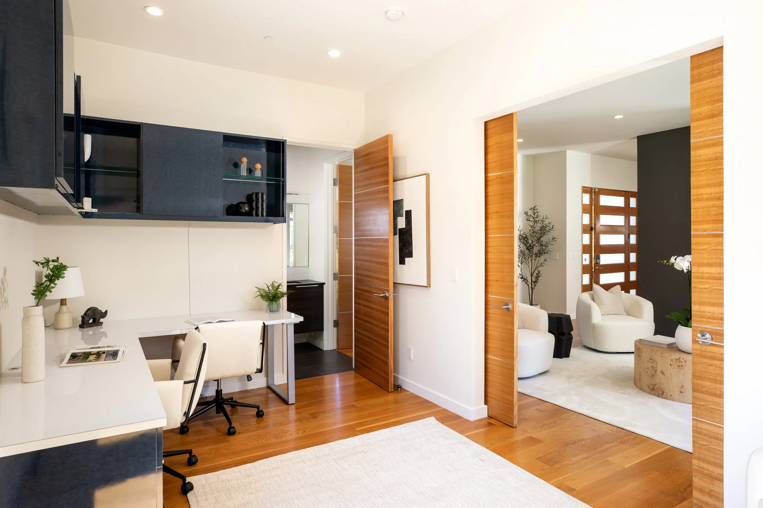 Living room with white chairs, a beige rug, and a corner with a dark accent wall and wooden door panels.