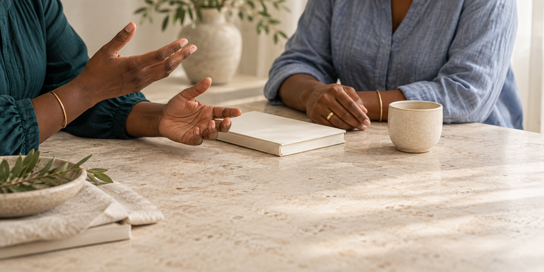 Two women having a conversation at a table with a notebook and a coffee mug.