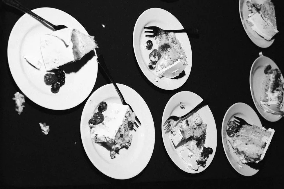 Multiple plates of partially eaten slices of cake with berries, and forks on a dark surface.