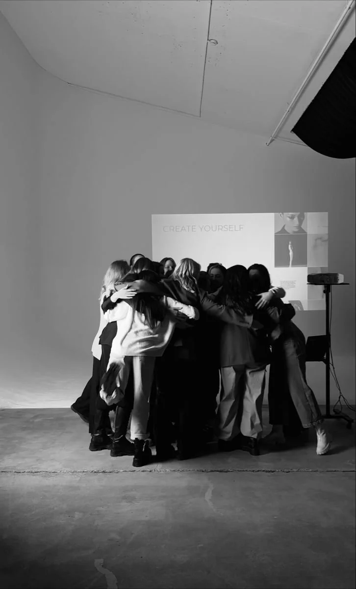 Group of people hugging each other in a photo studio with a projection on the wall that says "CREATE YOURSELF".