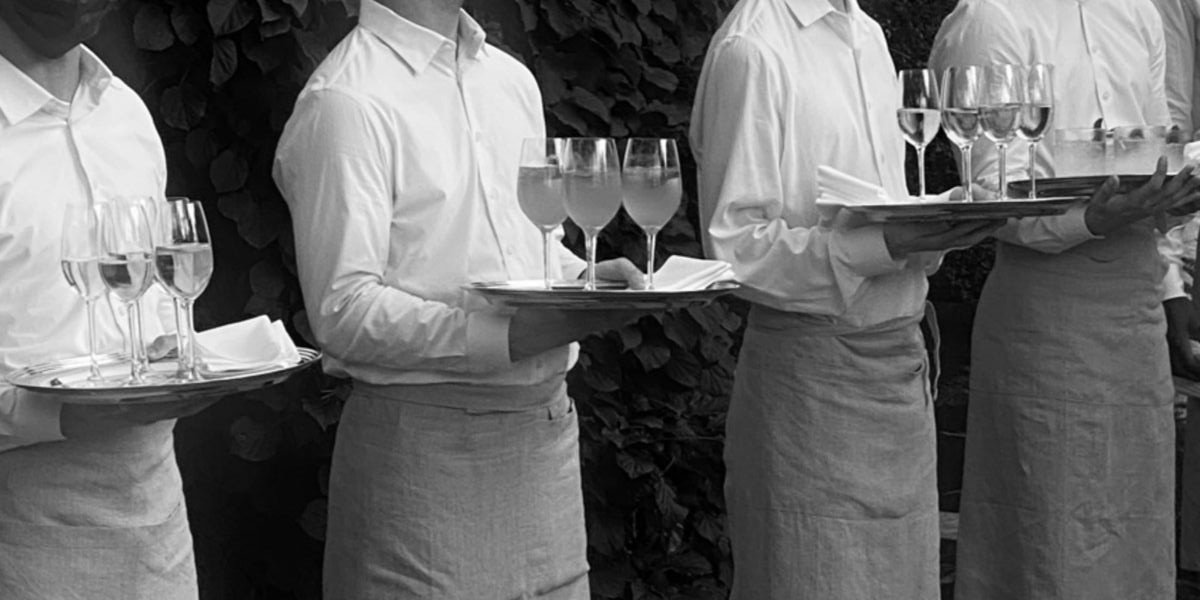 Four waitstaff members holding trays with wine glasses of different shapes and sizes during a formal event or dinner service.