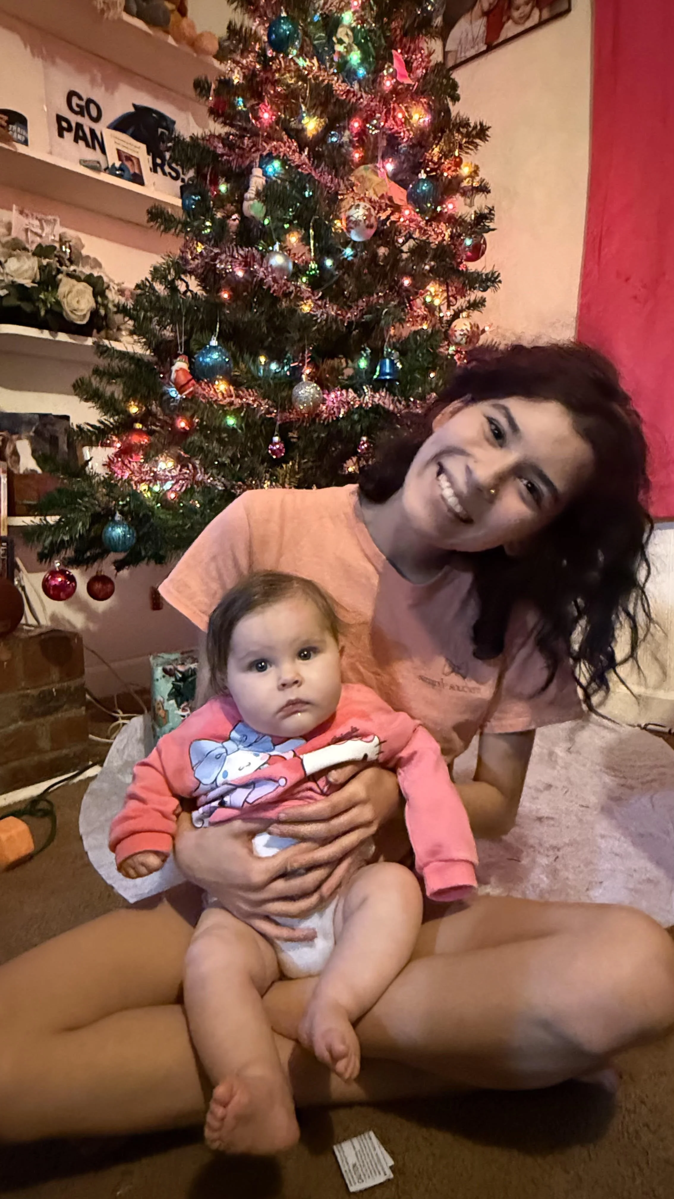 Makayla holding her niece in front of a decorated Christmas tree with colorful lights and ornaments.