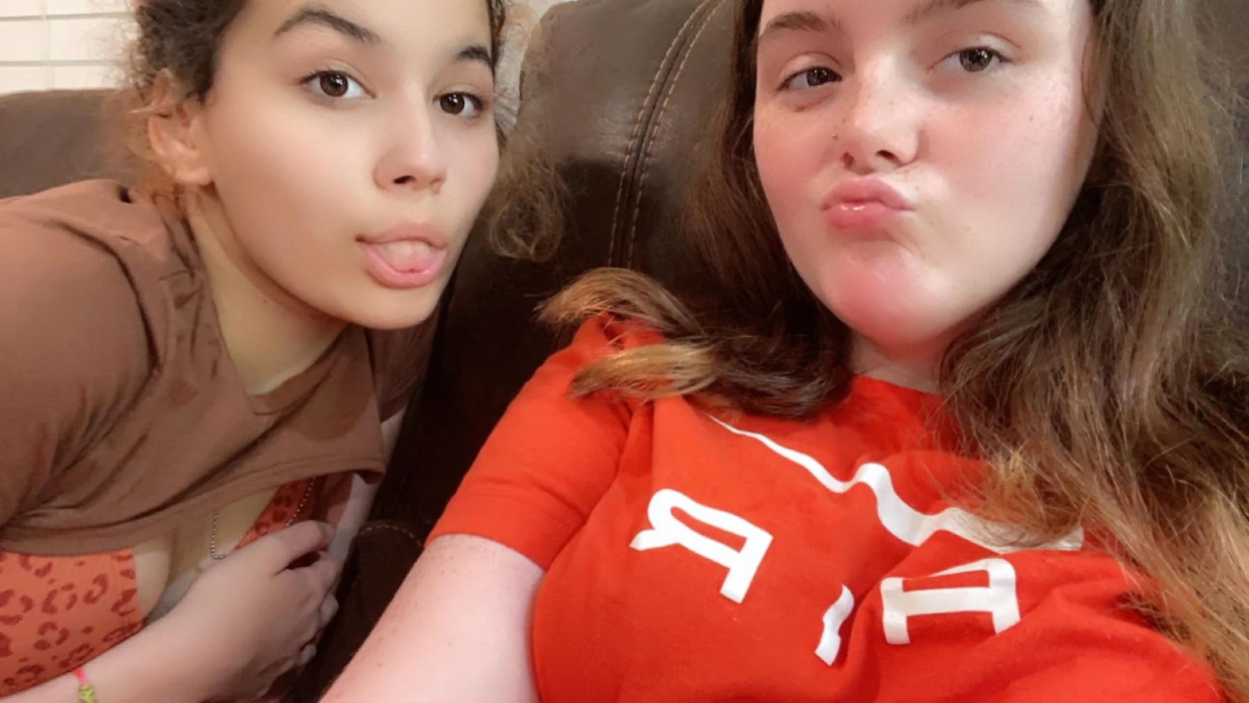 Makayla and her best friend. One is making a playful face with her tongue out, wearing a brown shirt, and the other is puckering her lips, wearing an orange shirt.