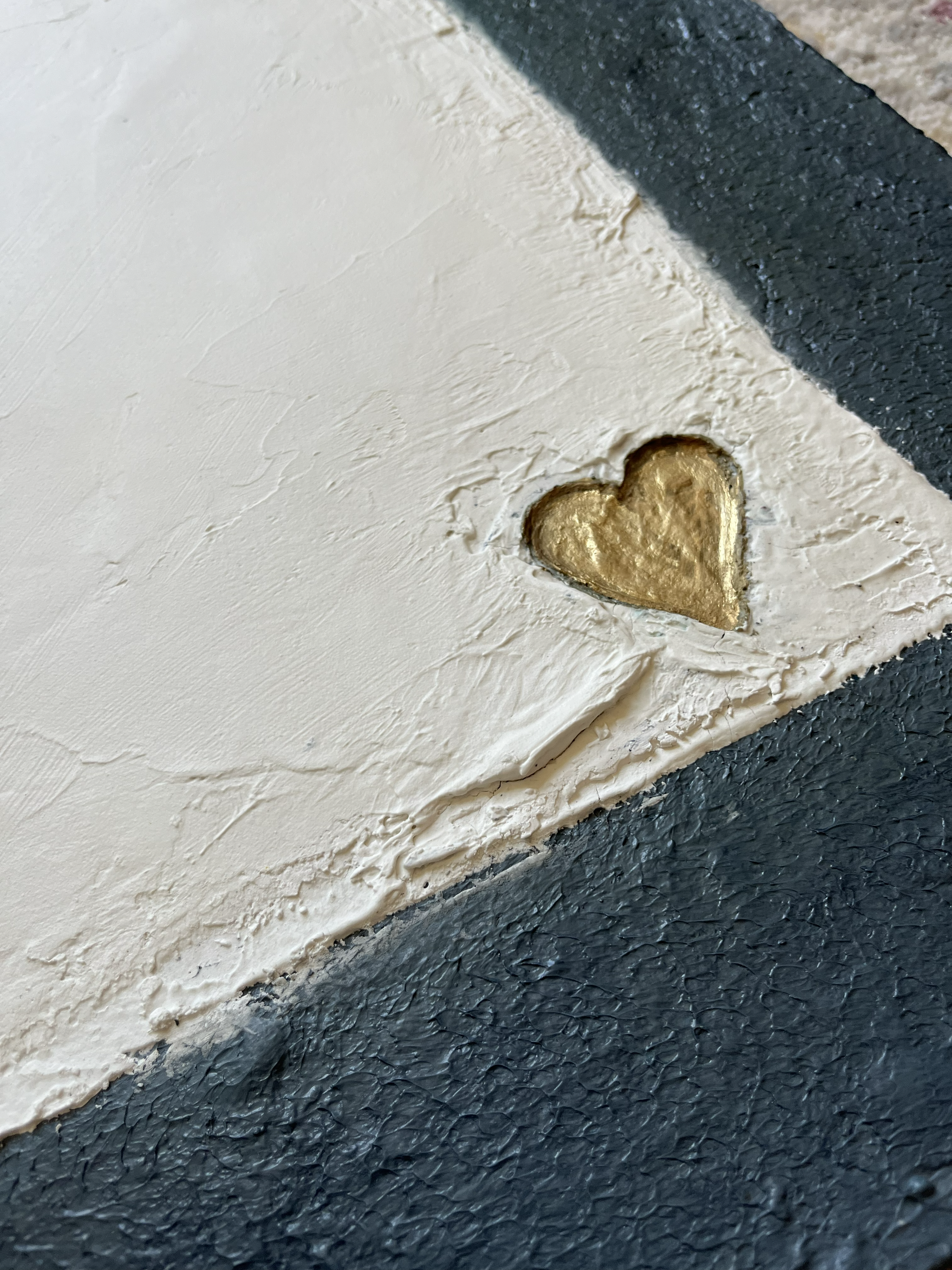 Close-up of a white textured surface with a small, gold metallic heart shape embedded in it, next to a black textured border.