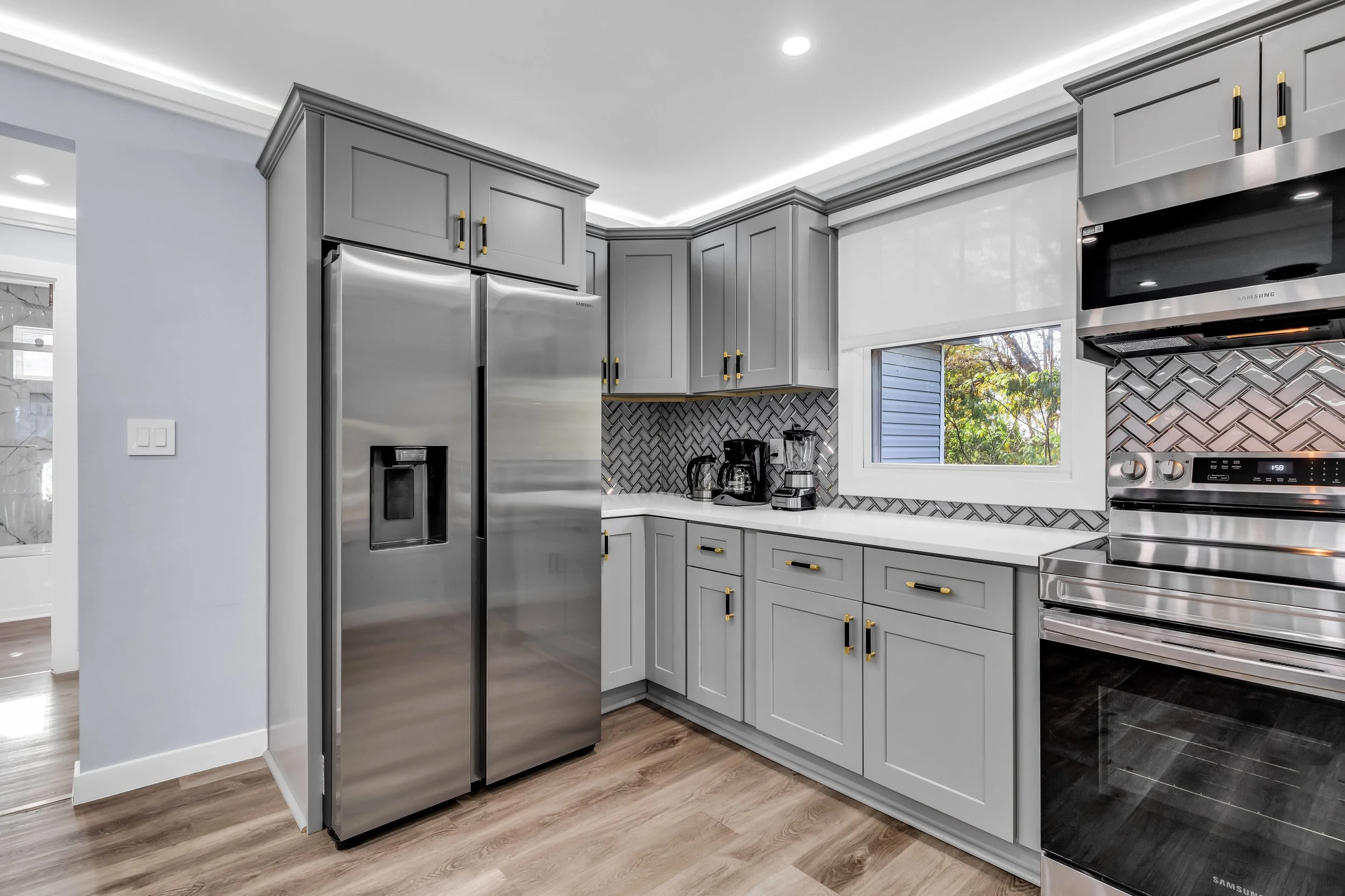 Modern kitchen with gray cabinets, stainless steel refrigerator, black and white herringbone backsplash, and stainless steel oven.