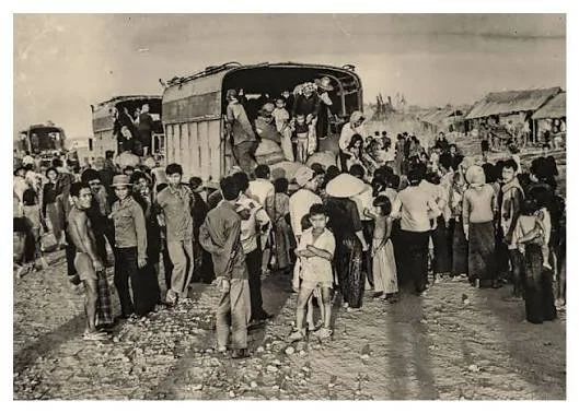 Black and white photo of a large group of people getting on and off a bus in a rural area, with some standing on the ground near the bus and others on the bus's open door.