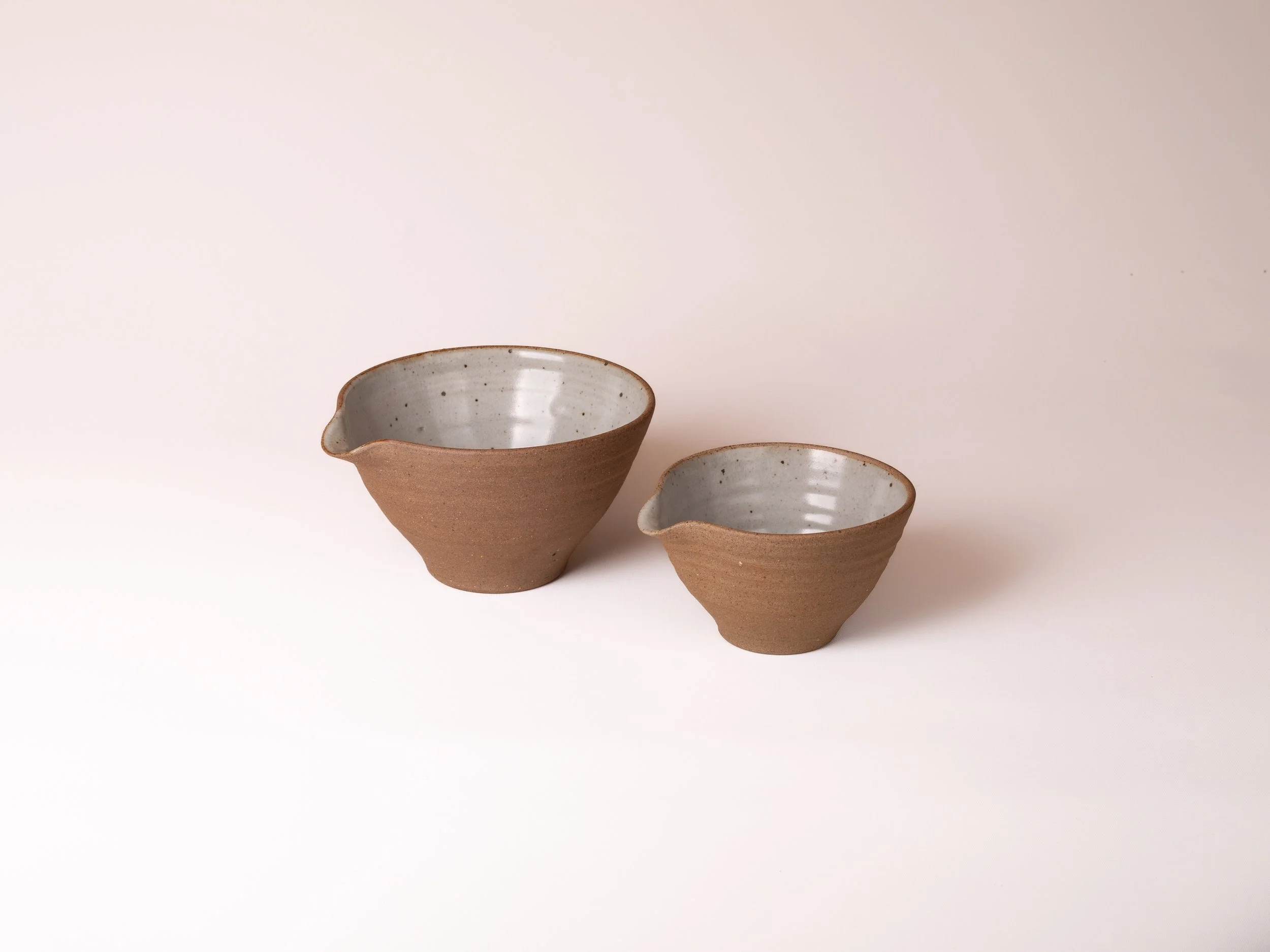 Two ceramic bowls with speckled gray insides and unglazed brown outsides on a white background.