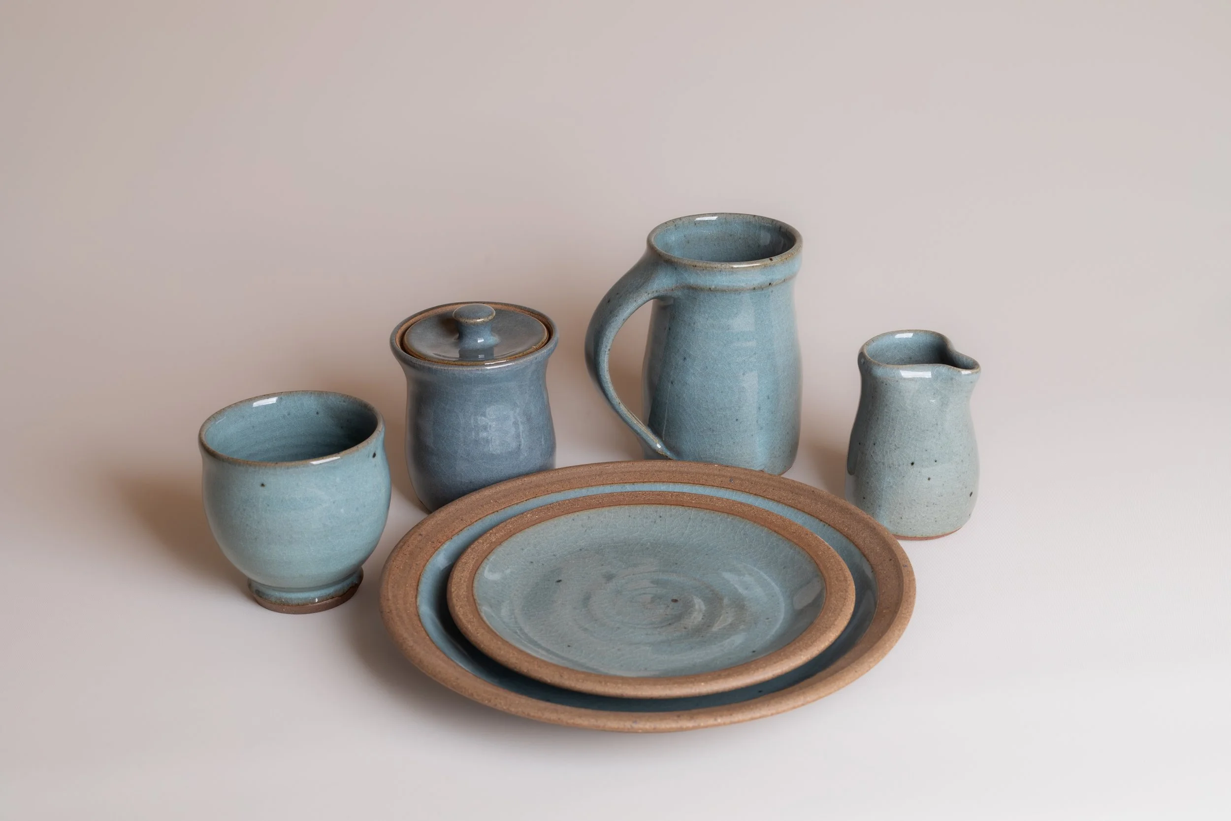 Collection of light blue ceramic dishware, including two small bowls, a tea pot, a creamer, and two saucers, arranged on a plain surface against a neutral background.