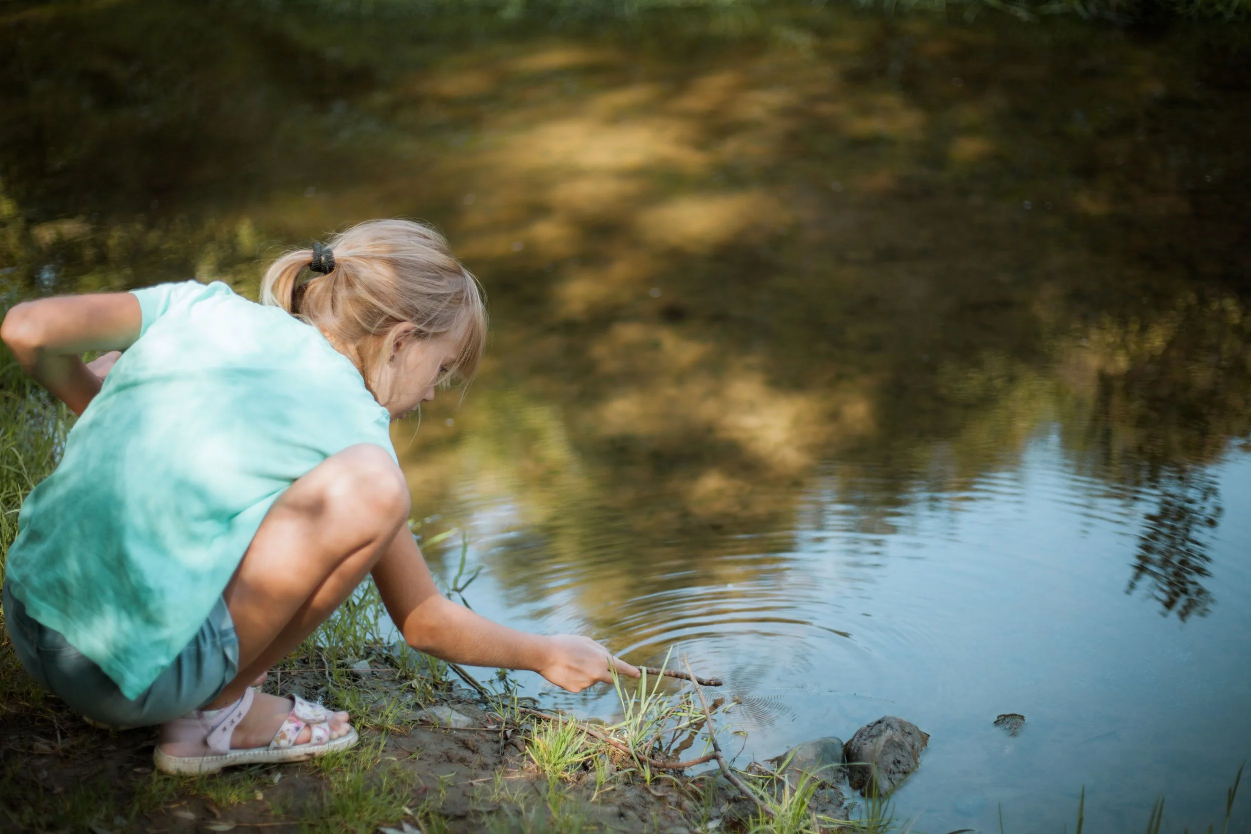 Girl touches a stick to the surface of the water