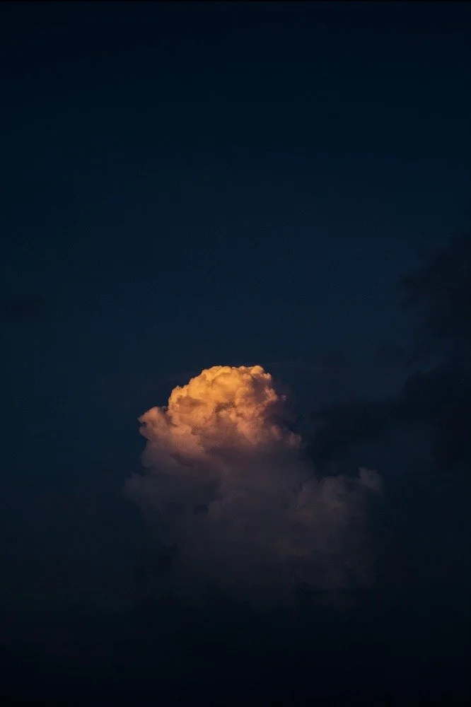 A single cloud illuminated with a warm, orange hue against a dark evening sky.