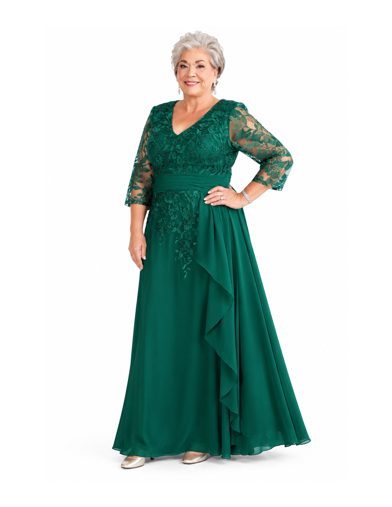 An older woman in an elegant green dress with lace detailing and a flowing skirt, standing against a plain white background with a confident pose, smiling slightly.