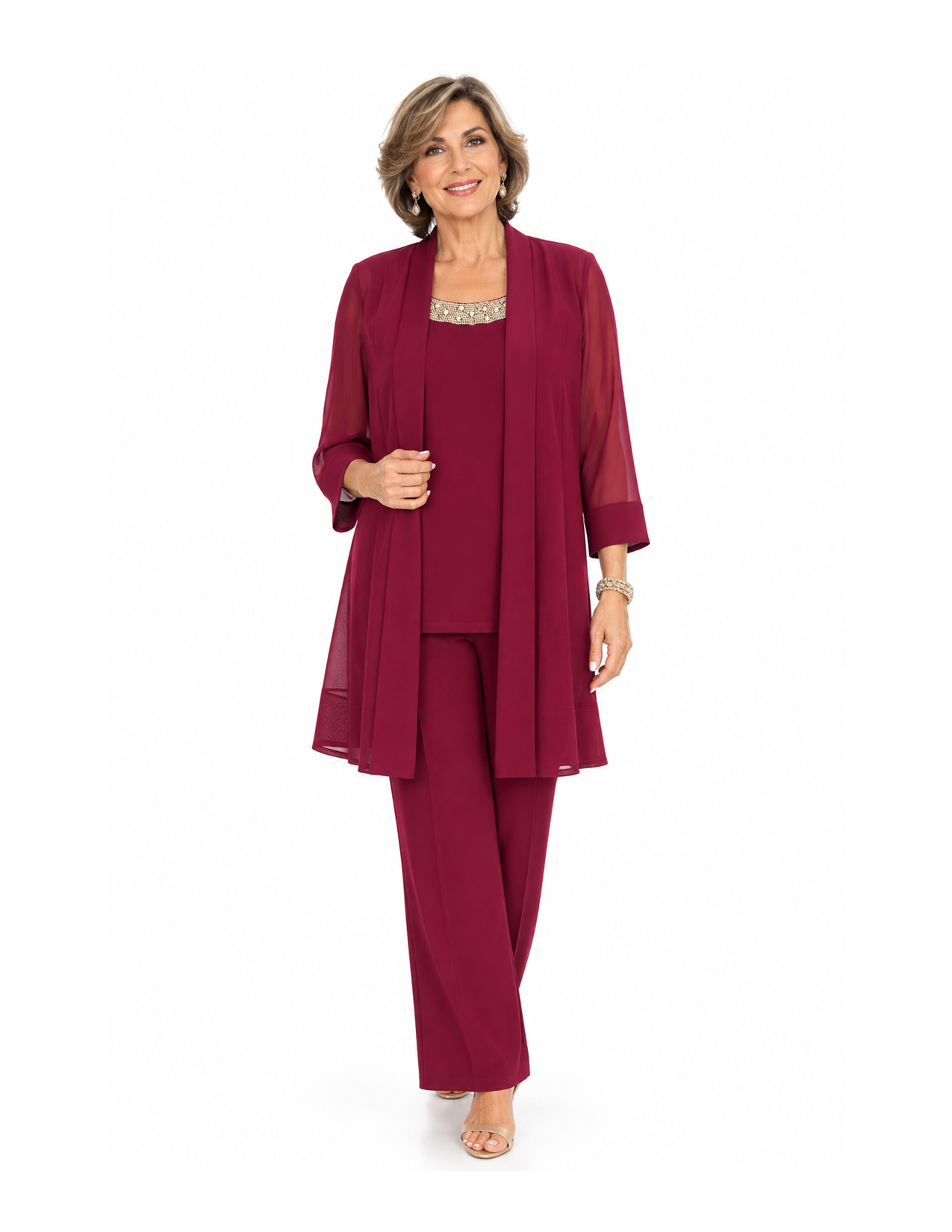 A woman in a burgundy matching suit with a sheer long coat and wide-leg pants, standing and smiling against a white background.