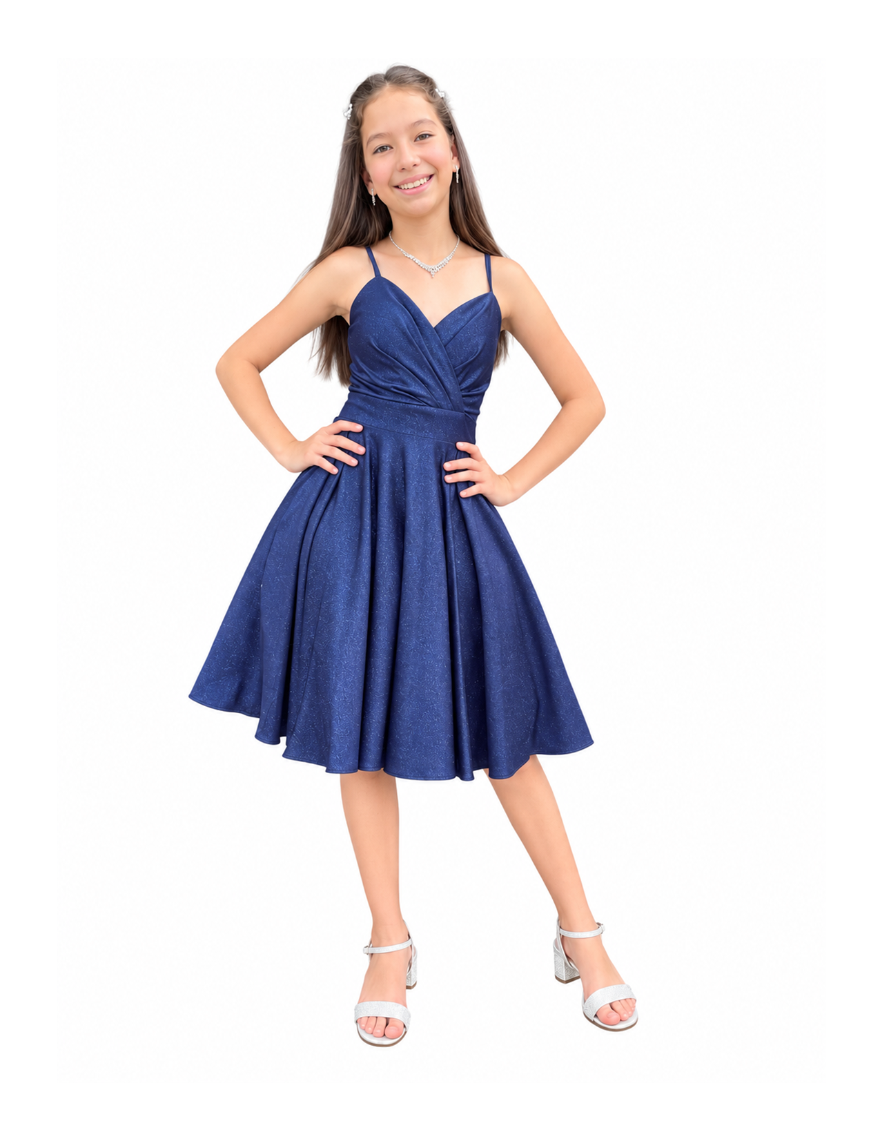 A girl wearing a sparkly blue dress with spaghetti straps, silver high heel shoes, and jewelry including earrings and a necklace, standing with hands on hips and smiling.