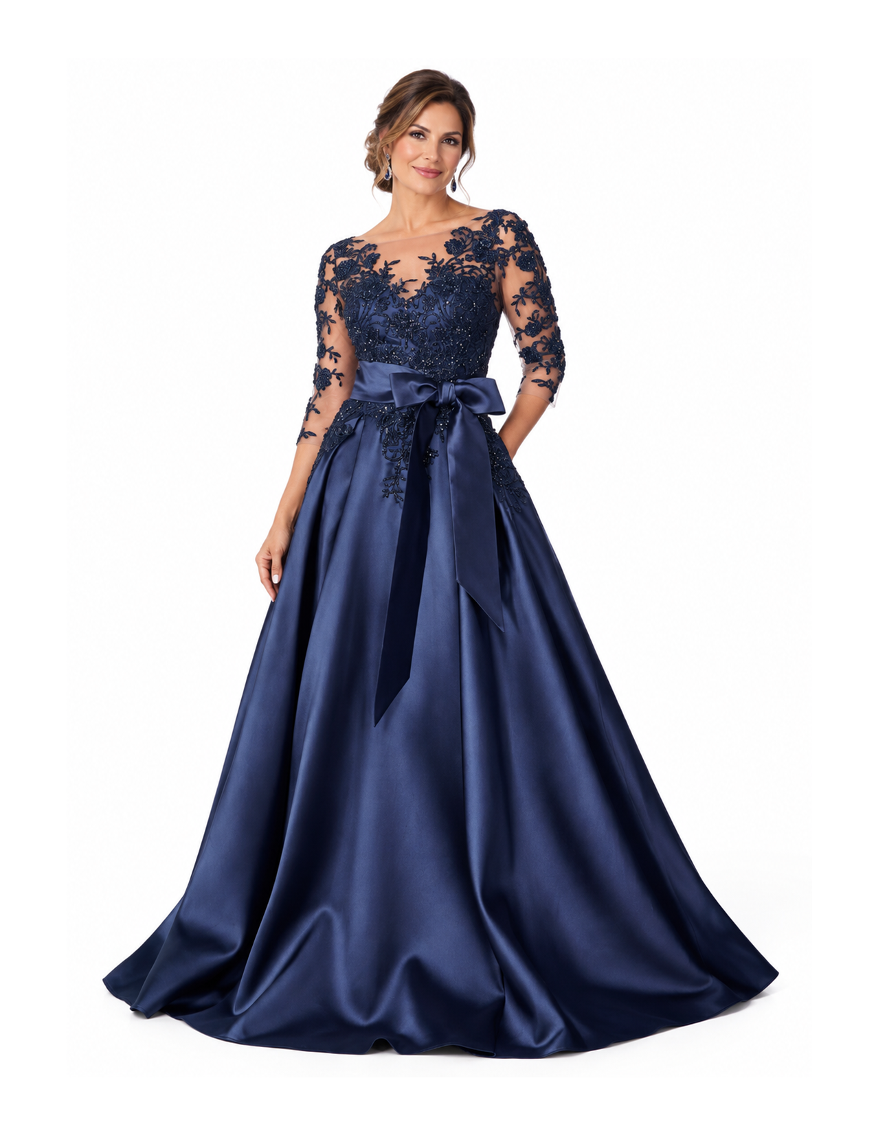 Woman standing in a long elegant navy blue gown with lace and floral embroidery on the bodice and sheer sleeves, a satin bow at the waist, and a full satin skirt.