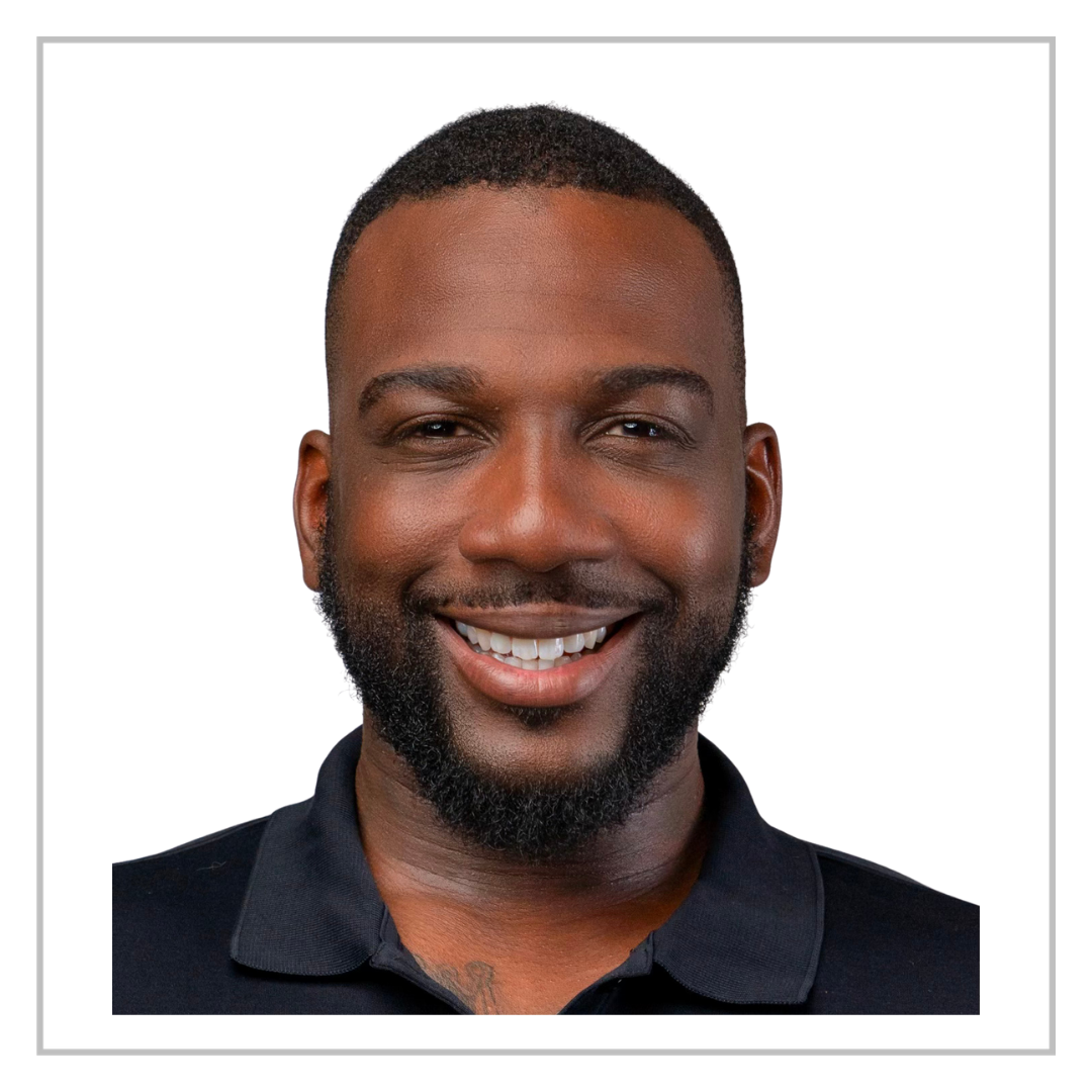 Portrait of a smiling African American man with short hair and a beard, wearing a black collared shirt.