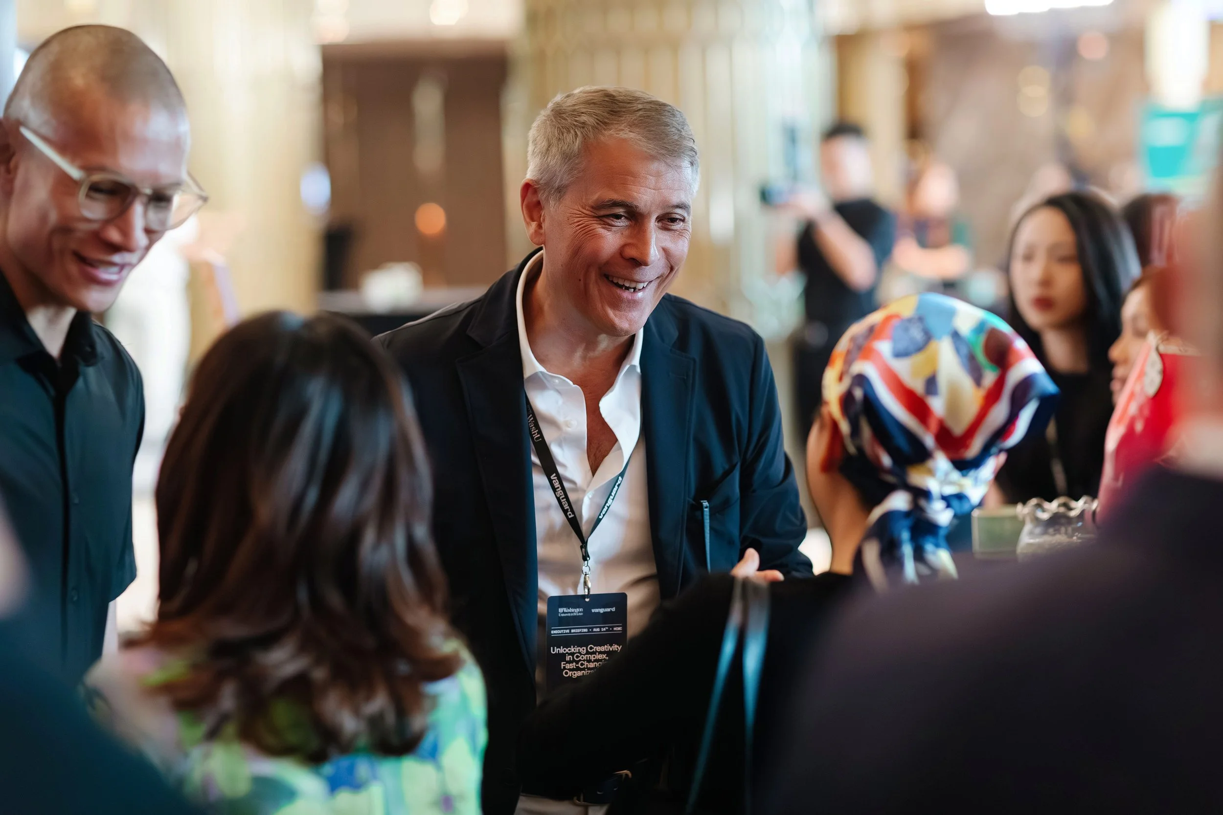 Man in white shirt and dark jacket smiling and talking to a woman wearing a colorful headscarf at a networking event.