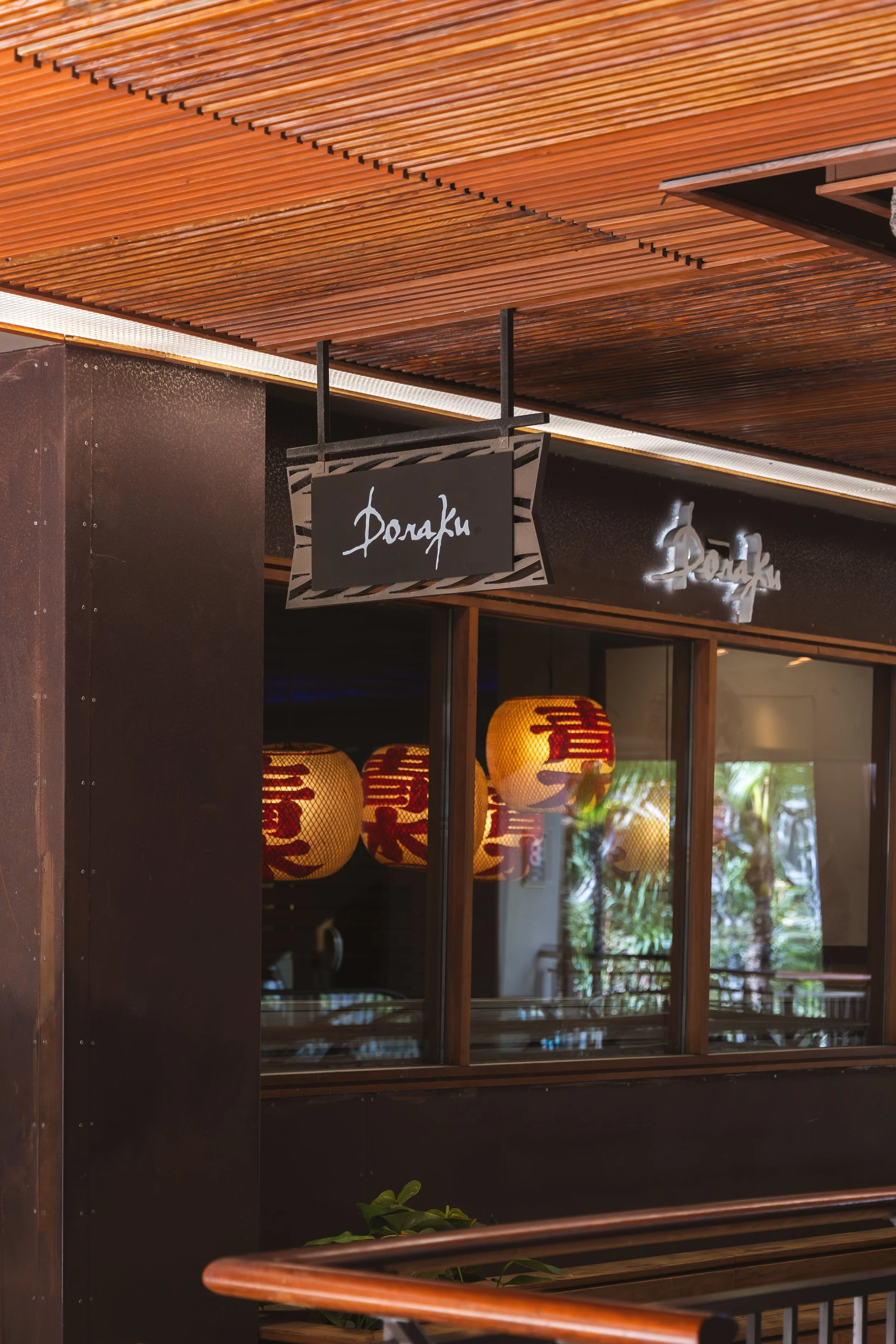Storefront with wooden exterior, hanging signs with Asian scripts, illuminated paper lanterns, and interior visible through window and glass door.