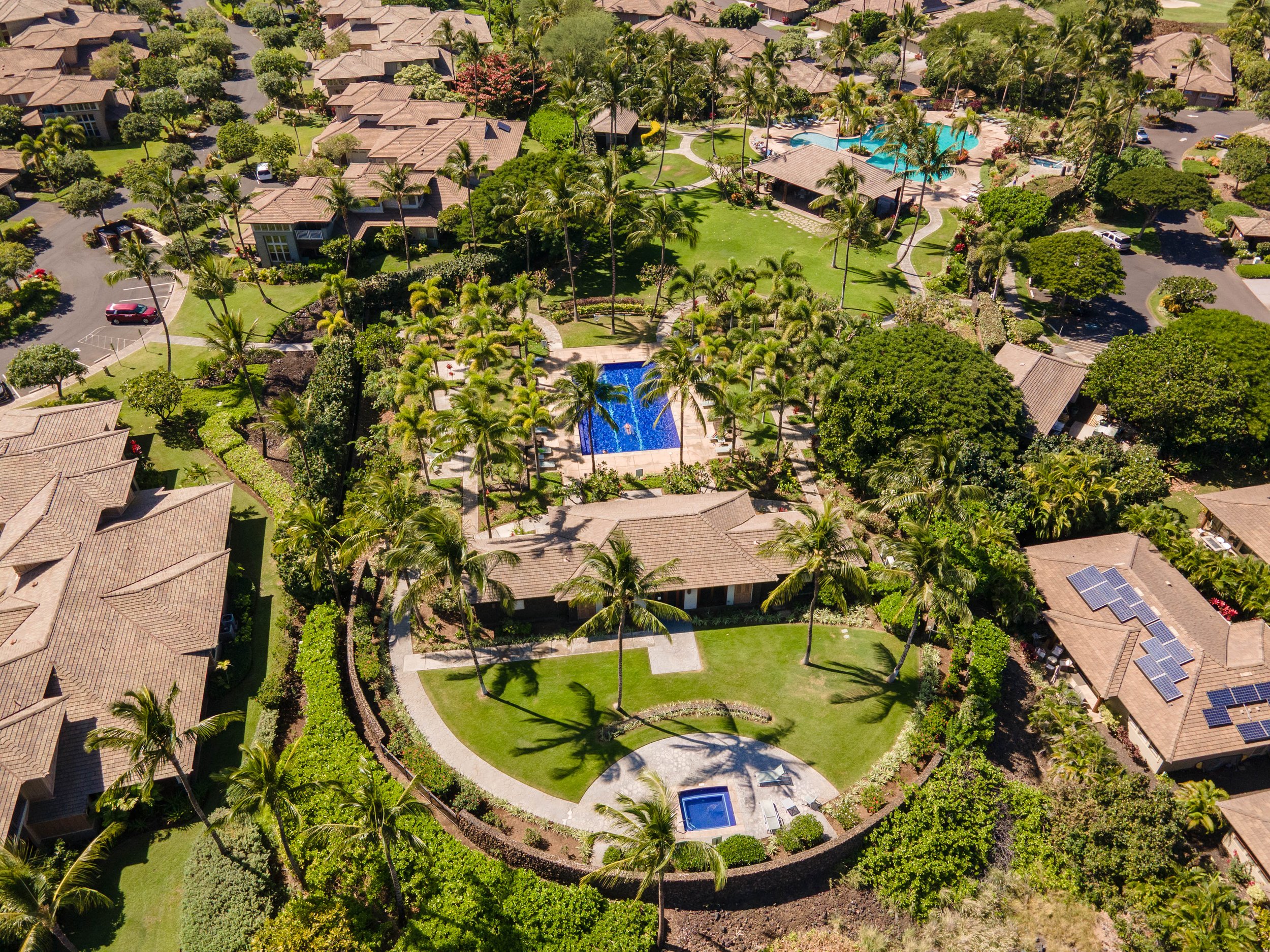 Aerial view of a residential community with apartment buildings, a swimming pool, walking paths, and landscaped gardens and palm trees.