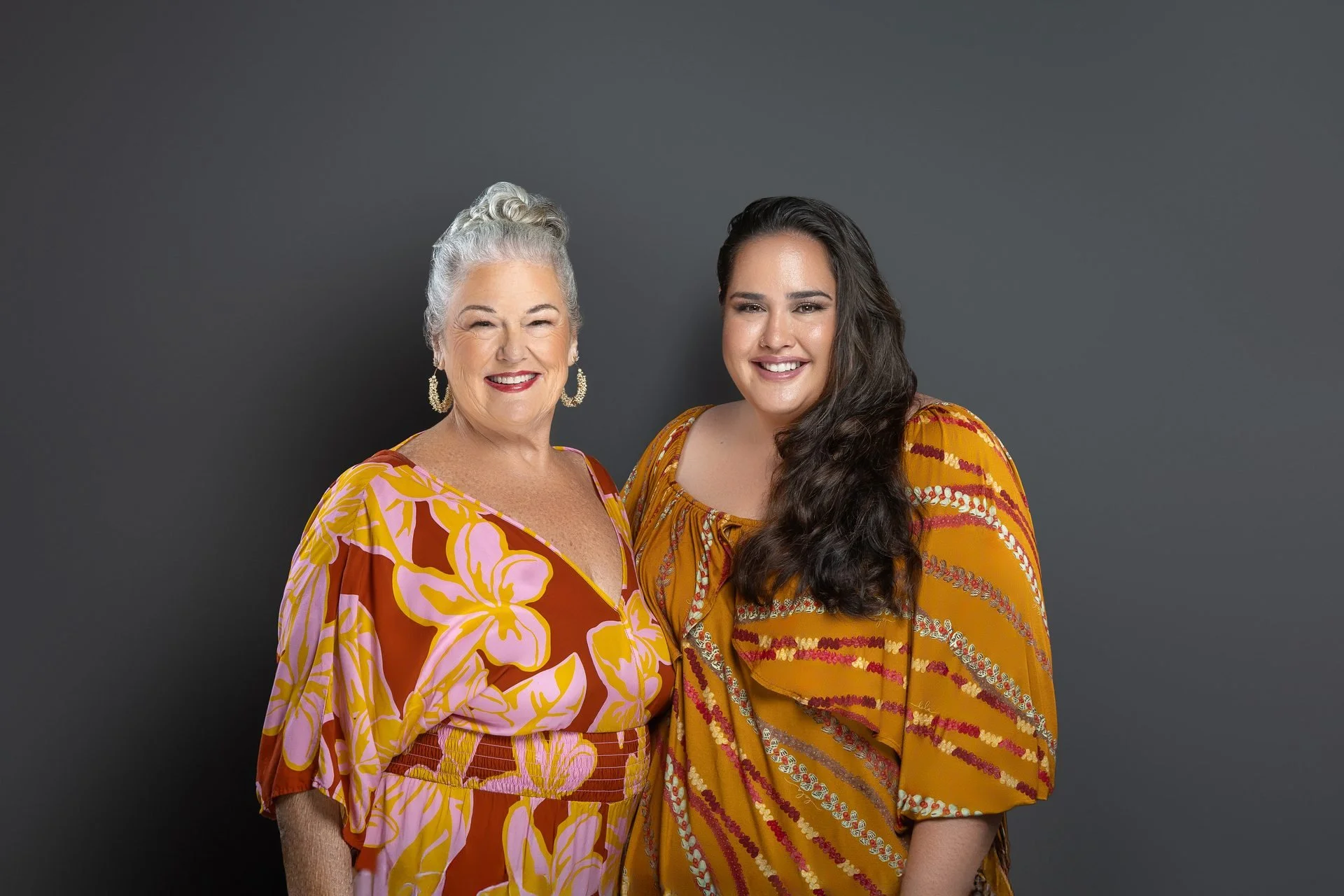 Professional headshots: two women in matching floral outfits on a dark gray backdrop
