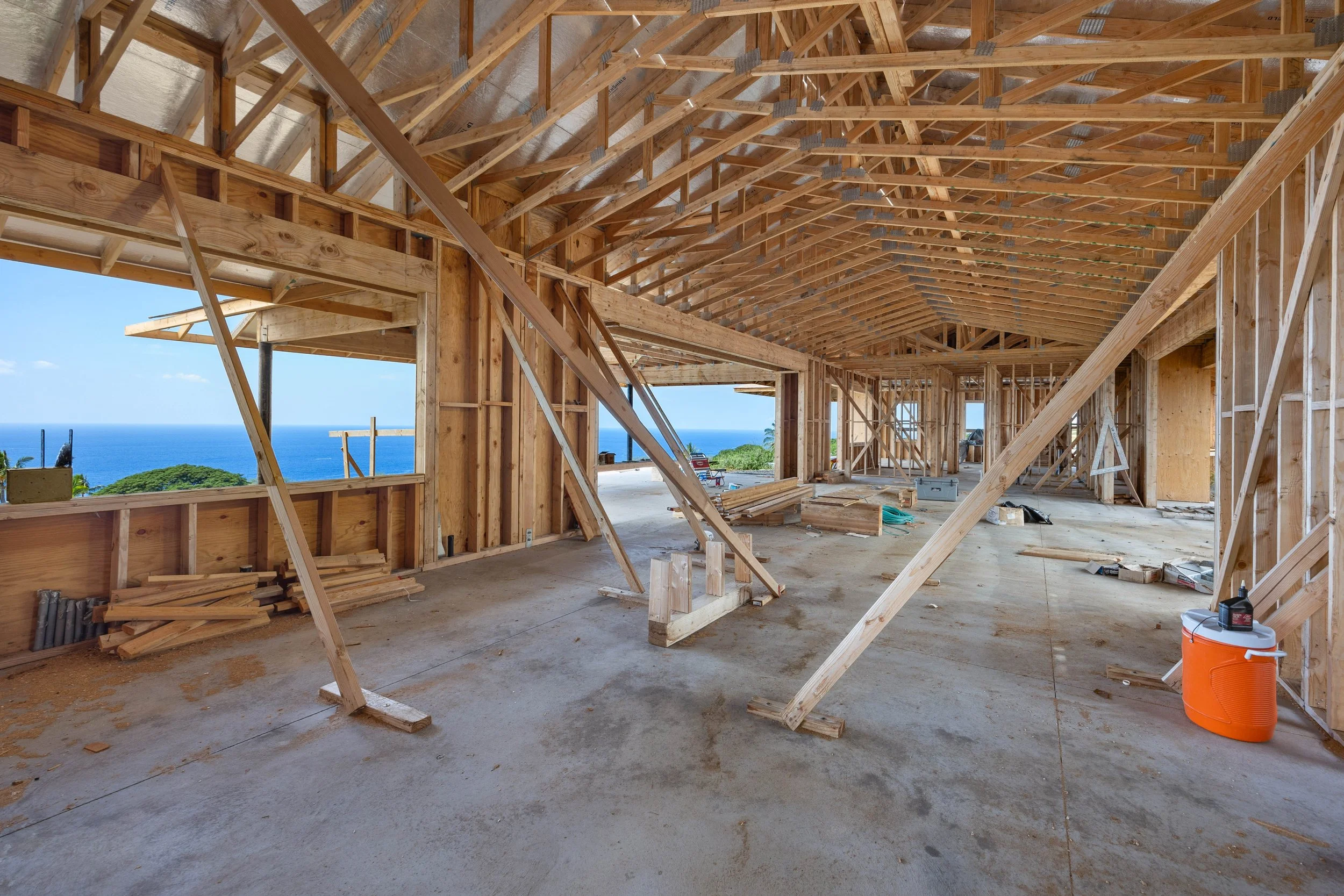 Construction site of a wooden house with framing and exposed beams, overlooking the ocean in the background.
