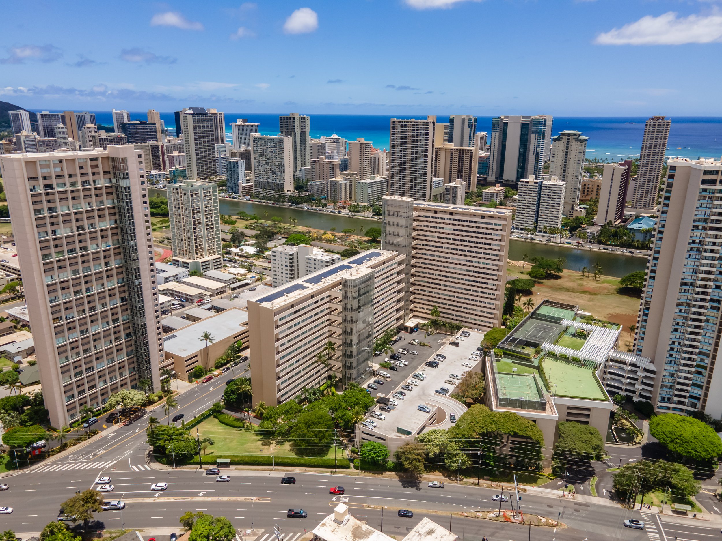 Aerial view of a city with numerous tall buildings near the coast, with a blue ocean and partly cloudy sky in the background.