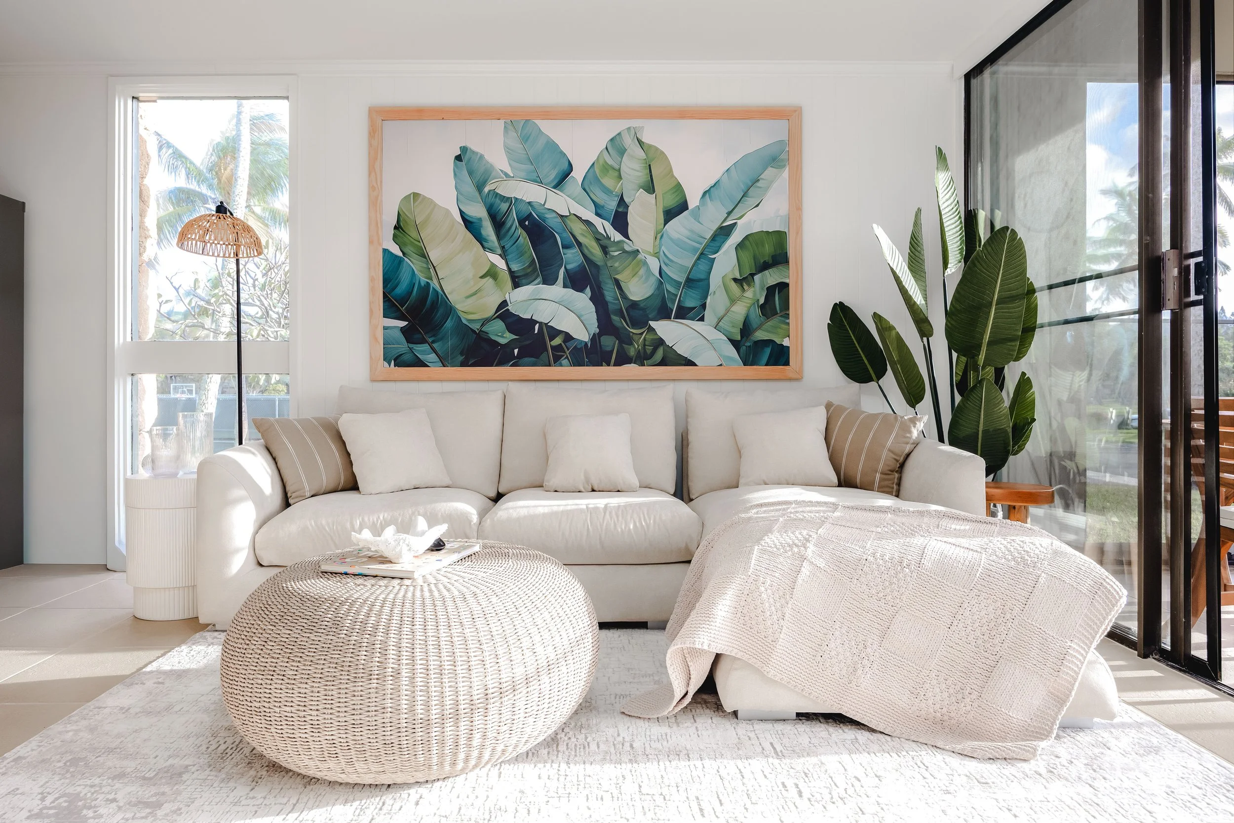 Bright living room with white couch, large botanical artwork, and tropical plants near glass sliding doors