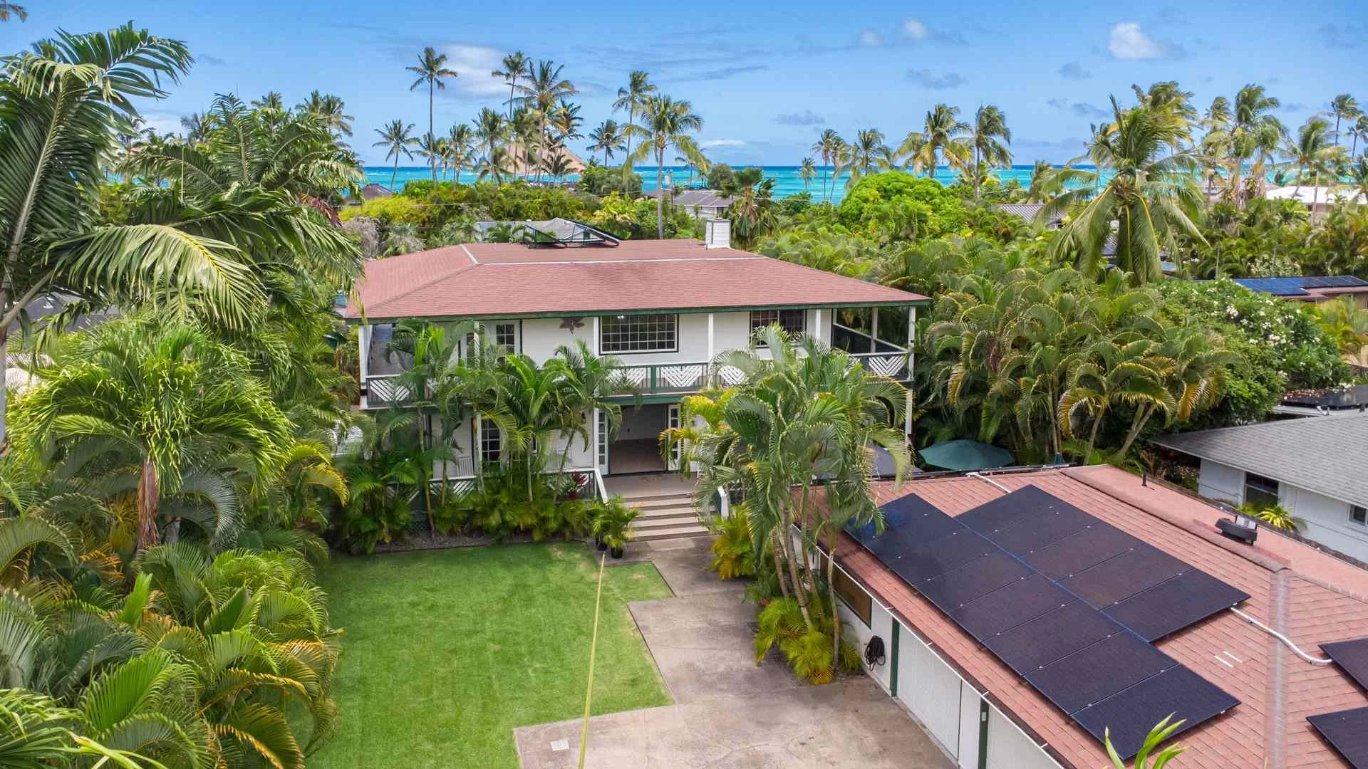 Drone photography and video: aerial view of a two-story home with red roof and tropical garden