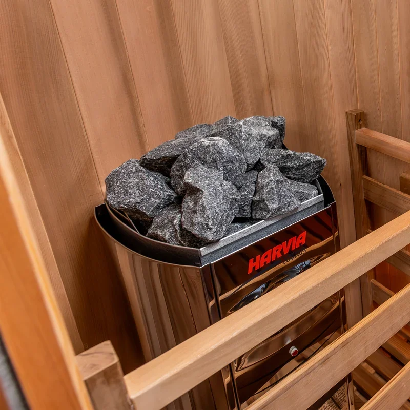 A sauna heater filled with large black rocks inside a wooden sauna room