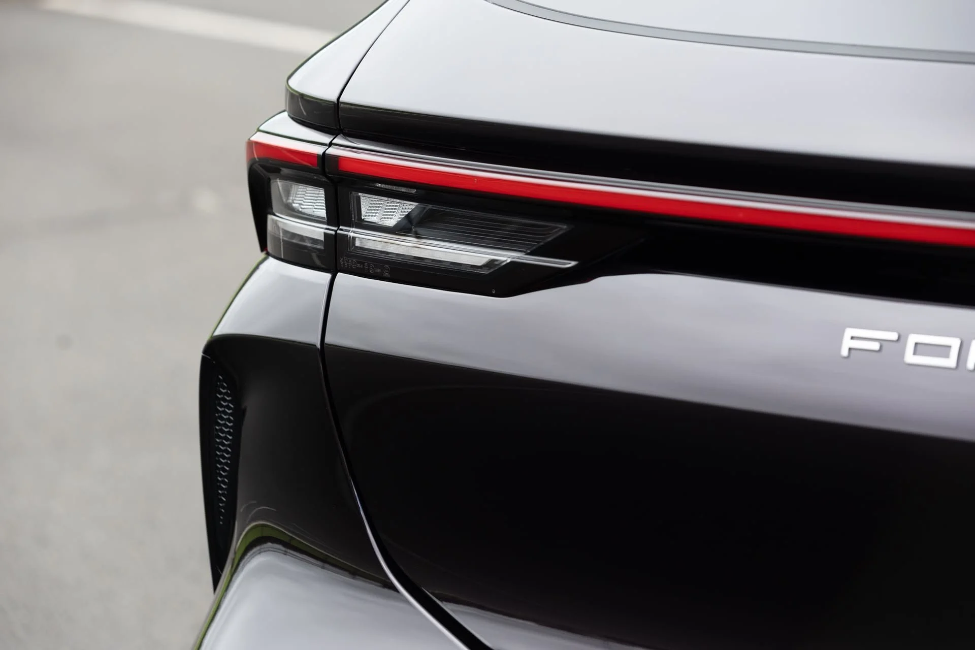 Close-up of a black car's rear with a modern tail light, a red strip, and part of the 'FO' letter visible, indicating a luxury vehicle.
