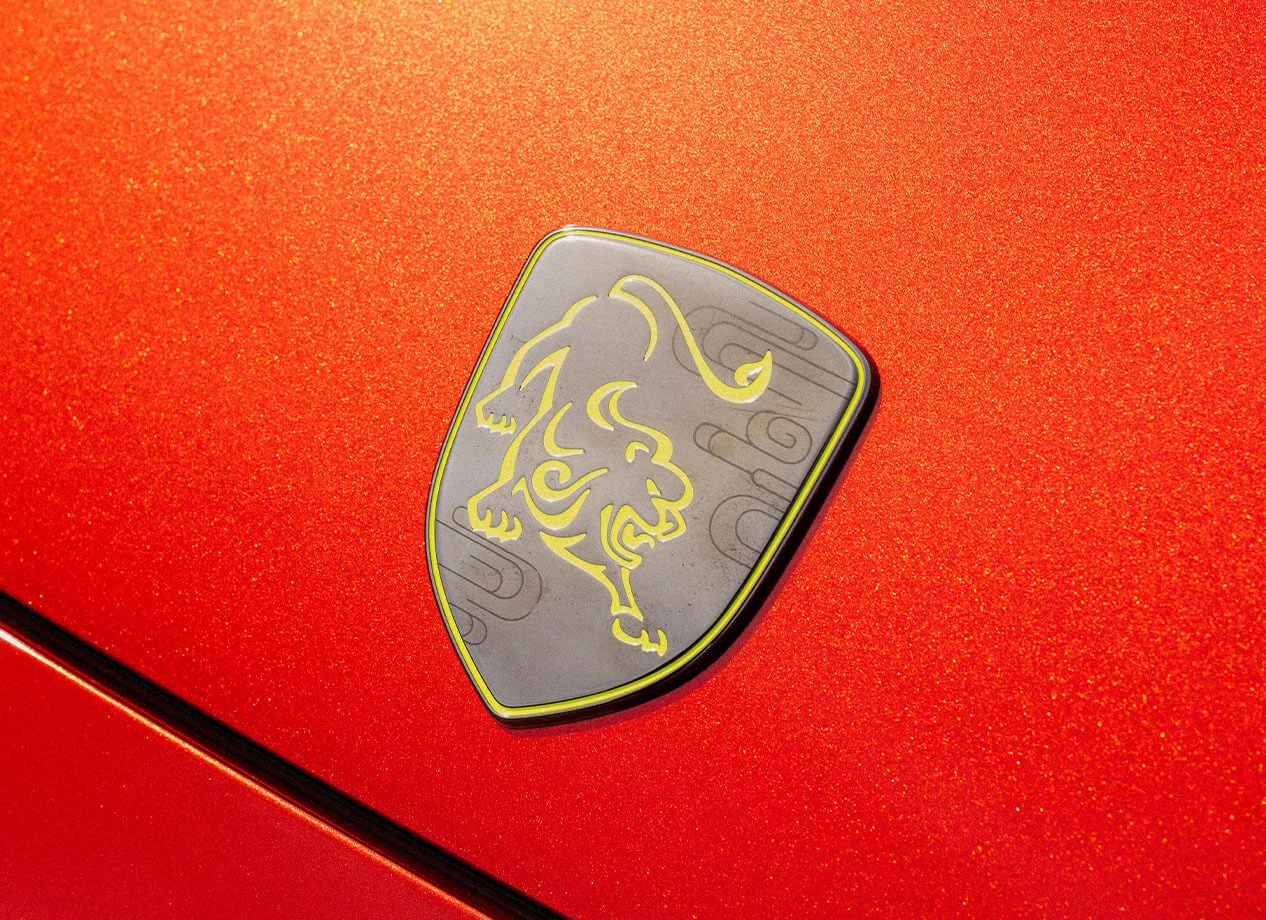 Close-up of a car badge with a lion logo on a red, metallic, glittery surface.
