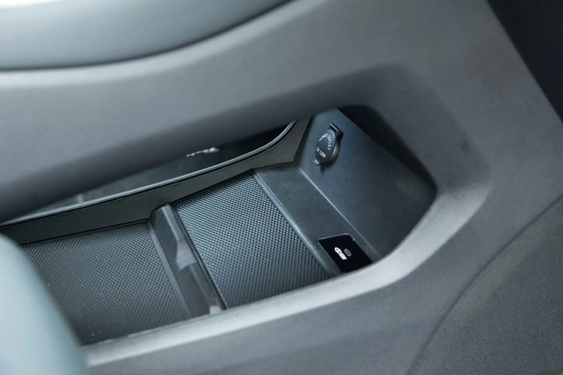 Close-up of a car's interior featuring an electronic device, a power outlet, and some textured surfaces on the center console.