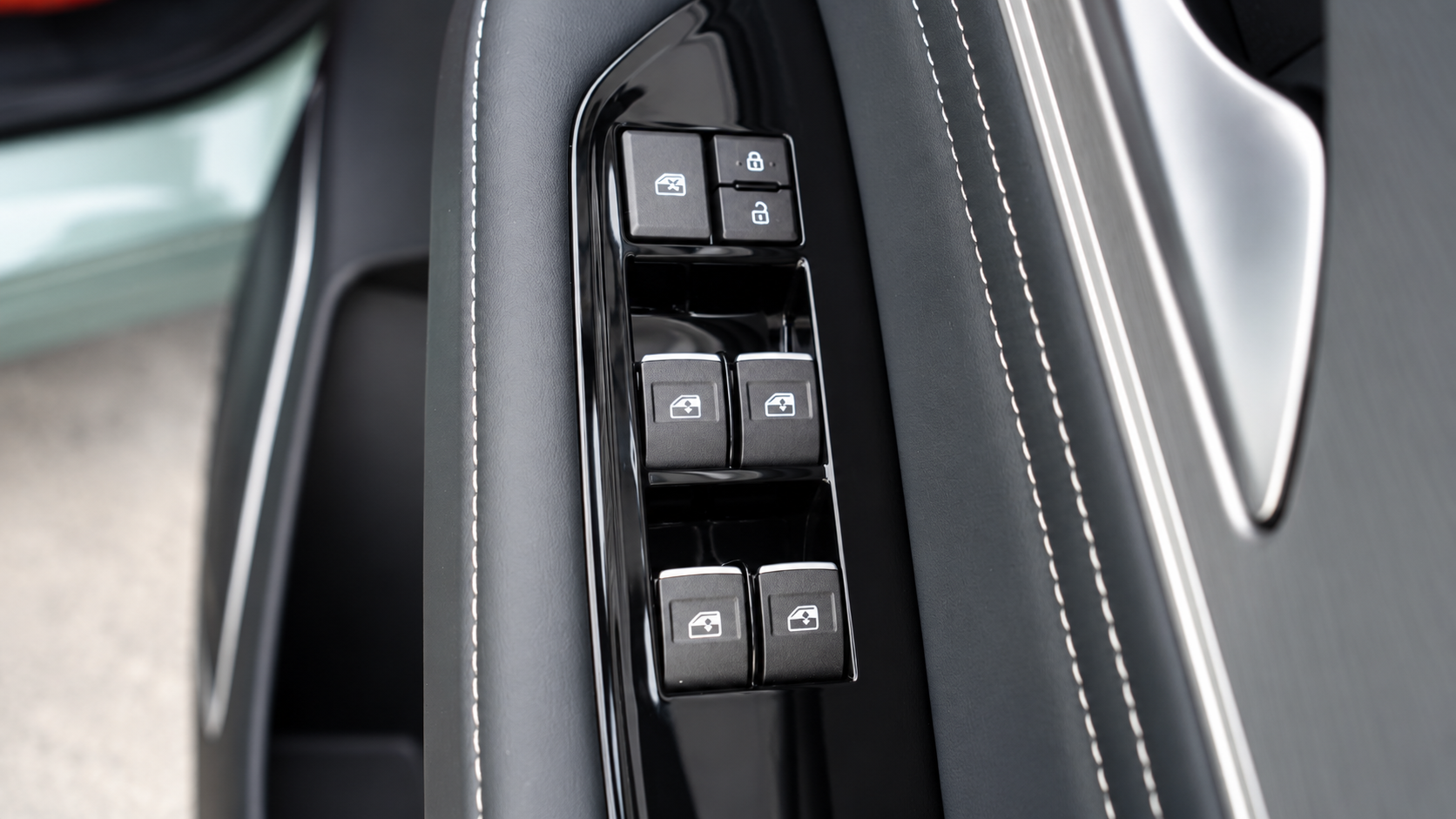 Close-up of a car's driver-side door control panel with window and lock switches on a black interior with white stitching.