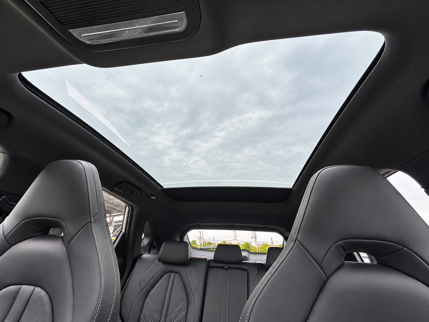 View of the interior of a car showing the front and rear seats with black upholstery, and a large panoramic sunroof revealing a cloudy sky.