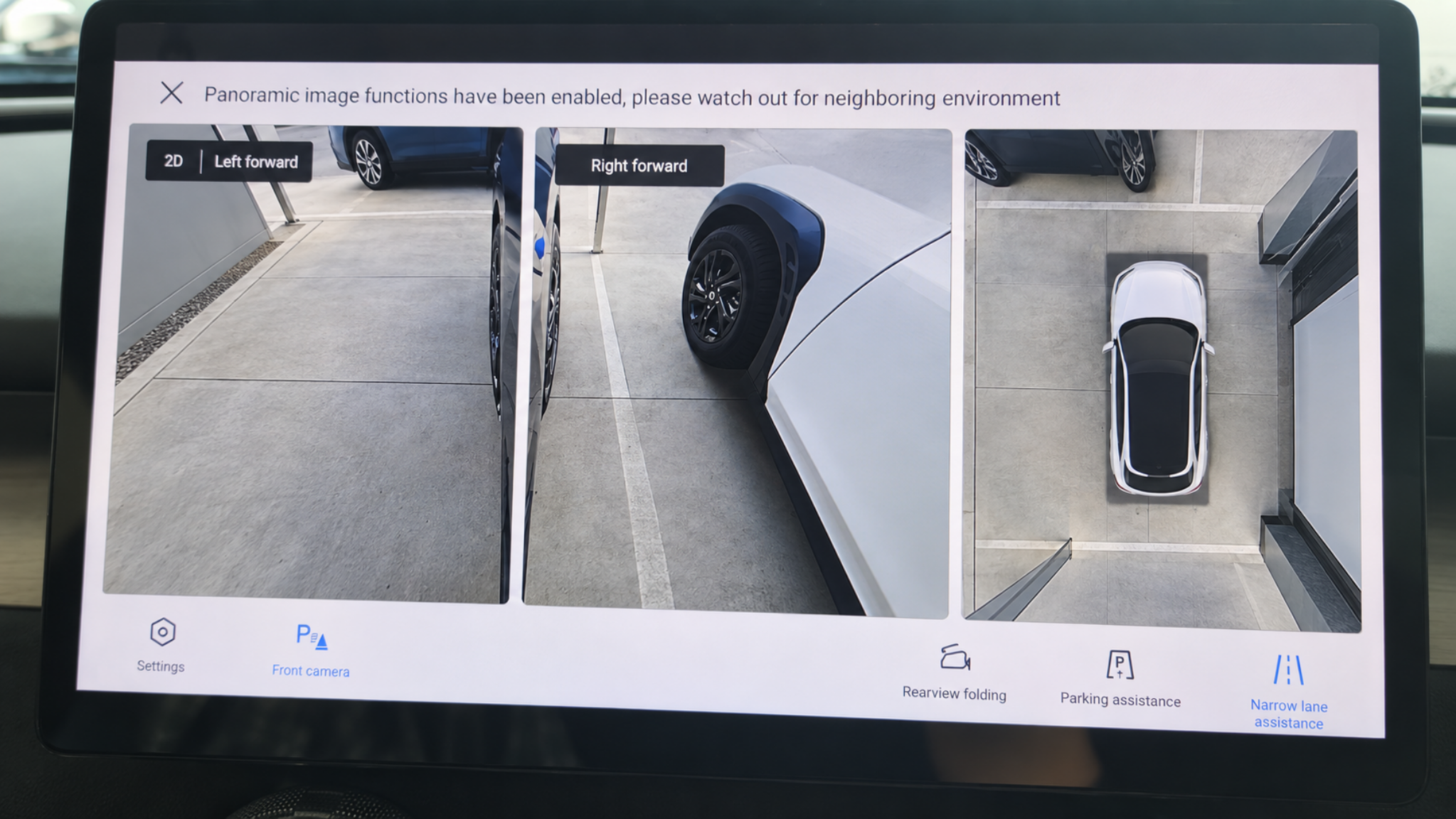 Display screen showing a 3D view of a parking lot with various car angles and surroundings, and menu options at the bottom.