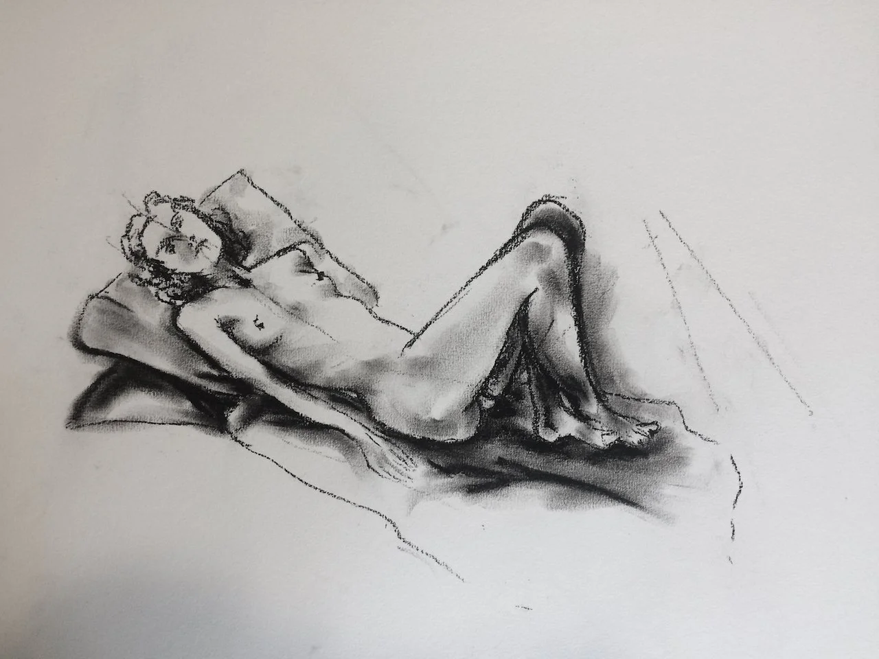 A black and white sketch of a woman lying on a bed with a pillow, looking at the viewer, with one arm resting on her side and one leg bent.