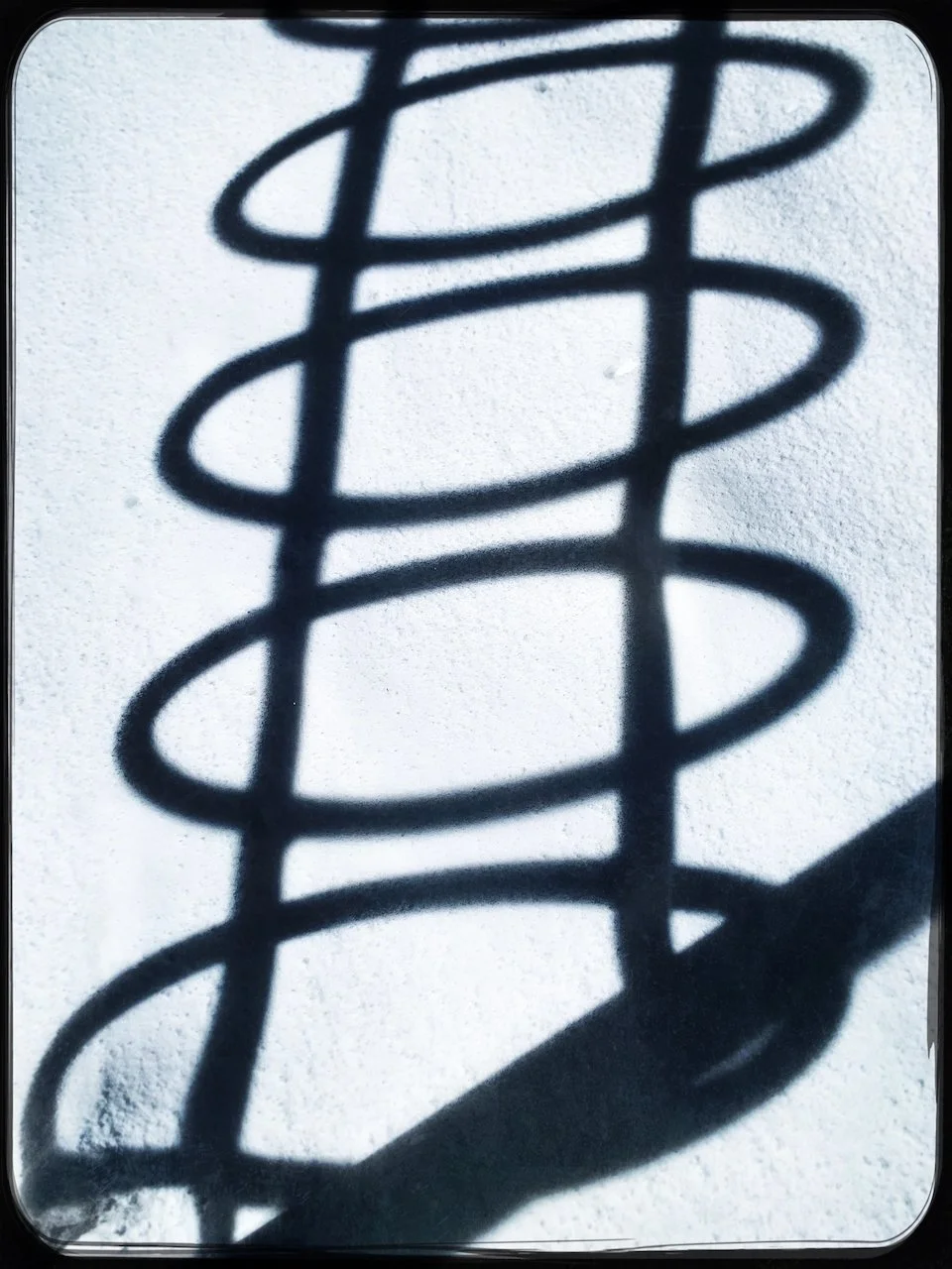 Shadow of a spiral-shaped metal structure cast on snow.