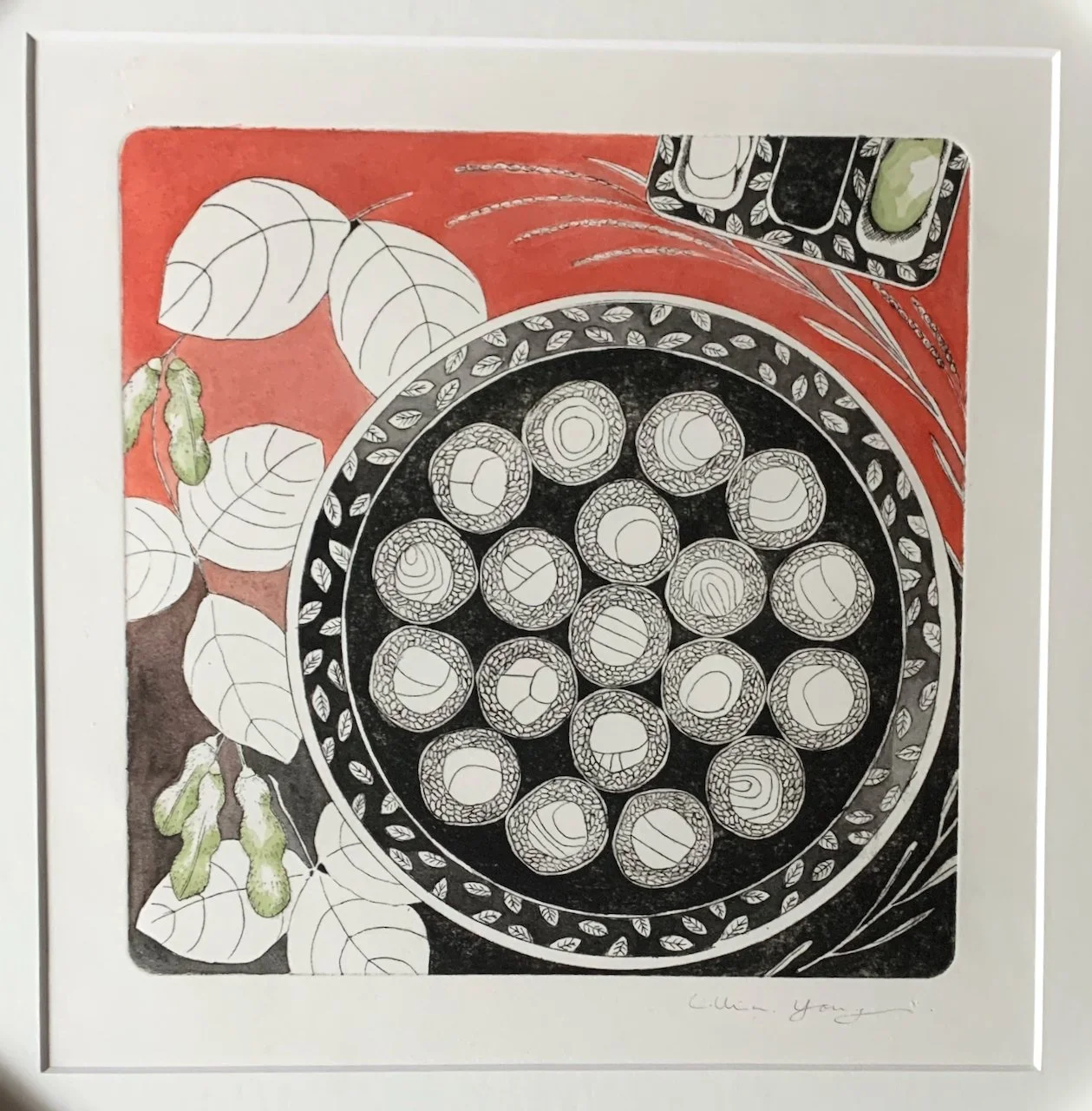 A framed artwork depicting a round black plate filled with sliced s, with a background of white and green leaves on a red backdrop, also including a small black dish with green food and a partially visible black and white patterned bowl or container.