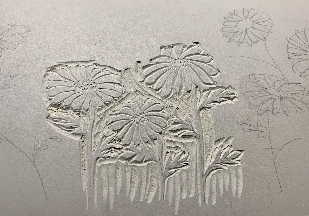 Partial drawing of flowers on paper with some flowers carved in white relief and others sketched with pencil.
