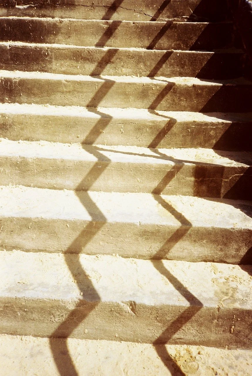 Concrete stairs with shadows cast by a zigzag-patterned railing or fence.