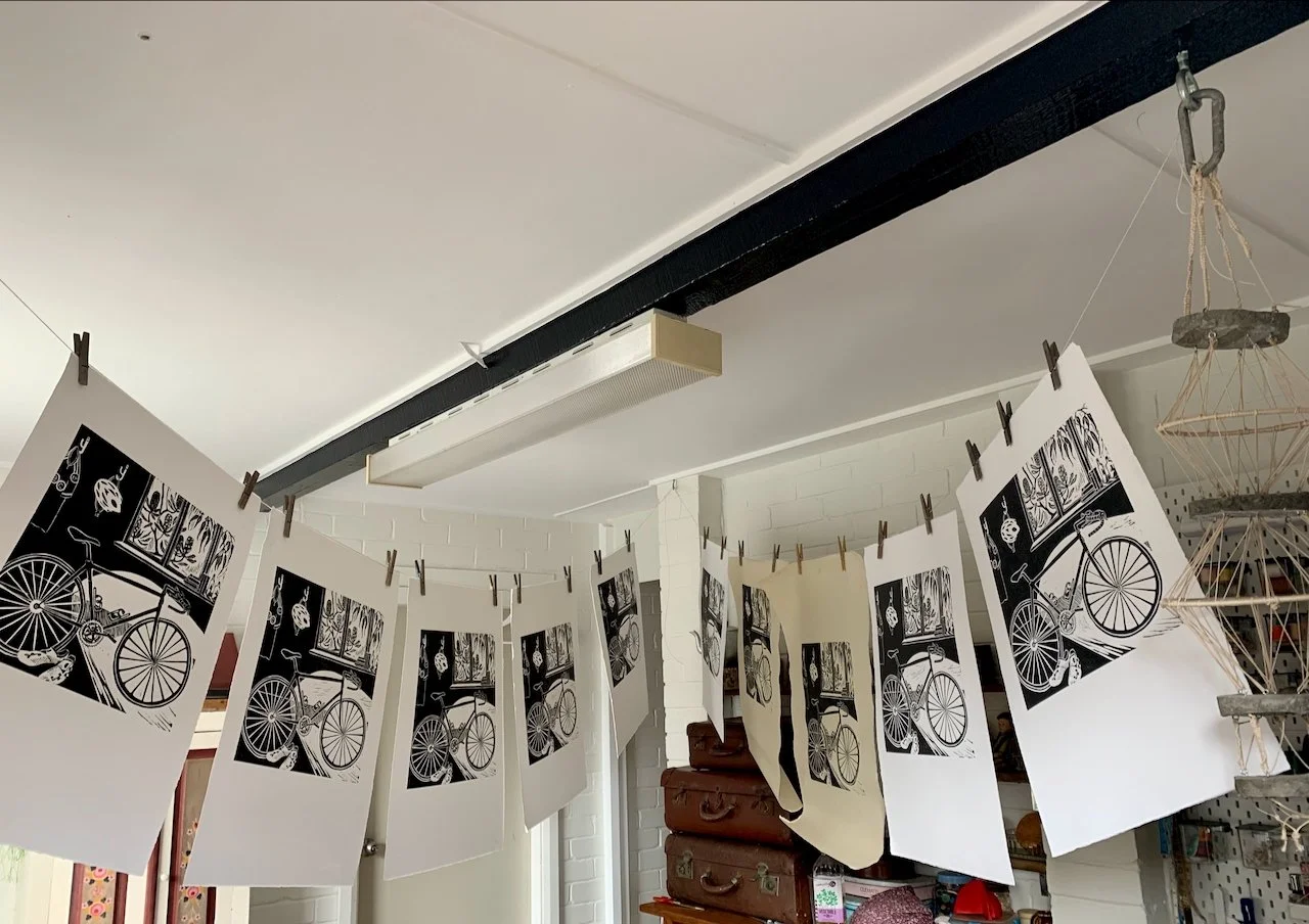 Black and white photographs of bicycles hanging on a clothesline with small clothespins inside a room.