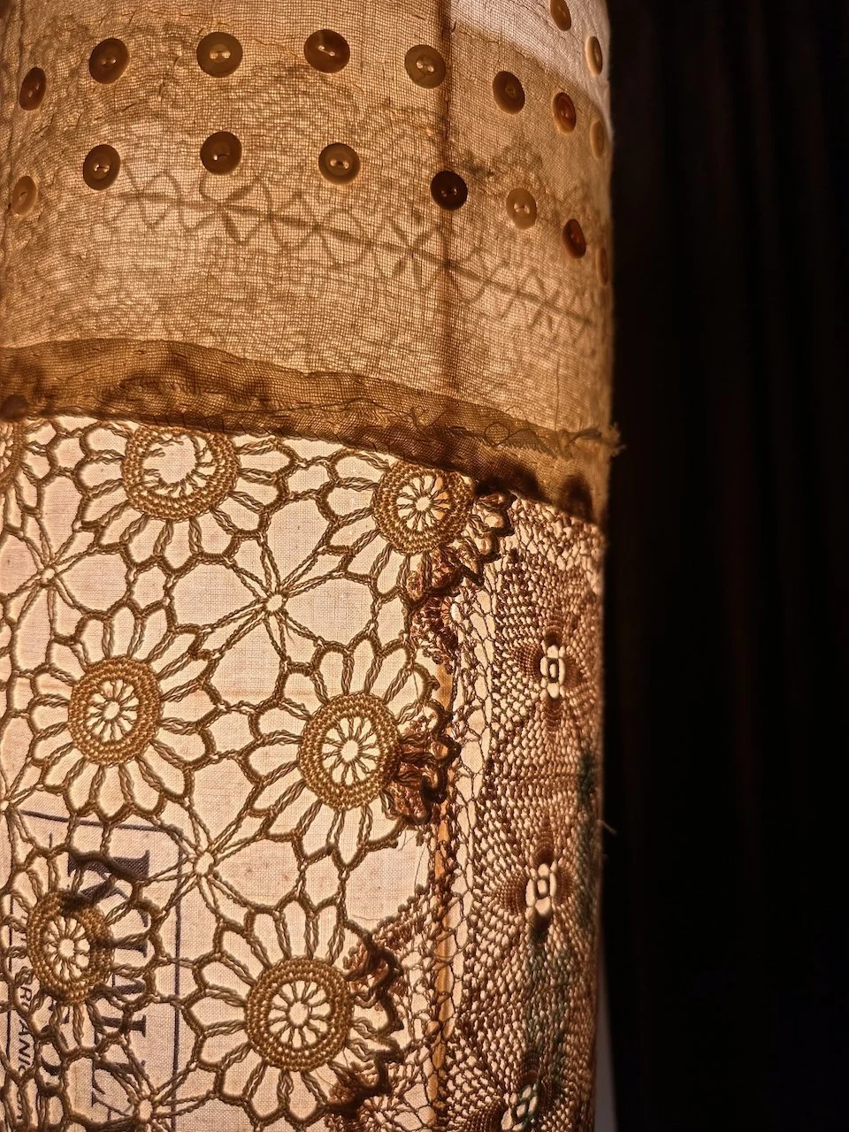Close-up of a fabric lampshade with lace and embroidered details, illuminated from inside.