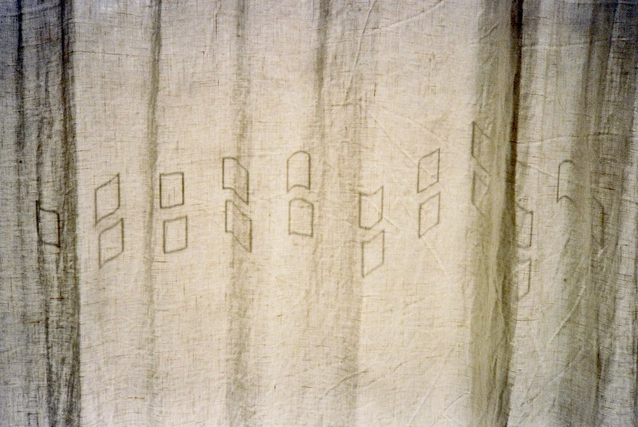 Close-up of a beige curtain with small geometric cutouts in the shape of rectangles and semi-arches.