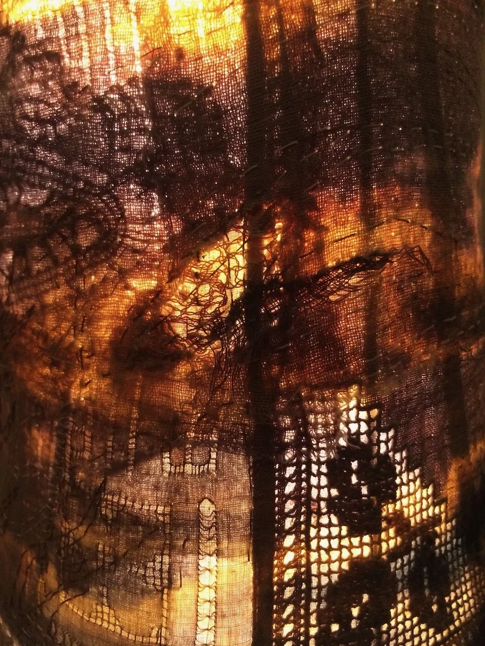 Close-up of a window screen with a fire burning behind it, showing flames and darkened areas of burnt material.