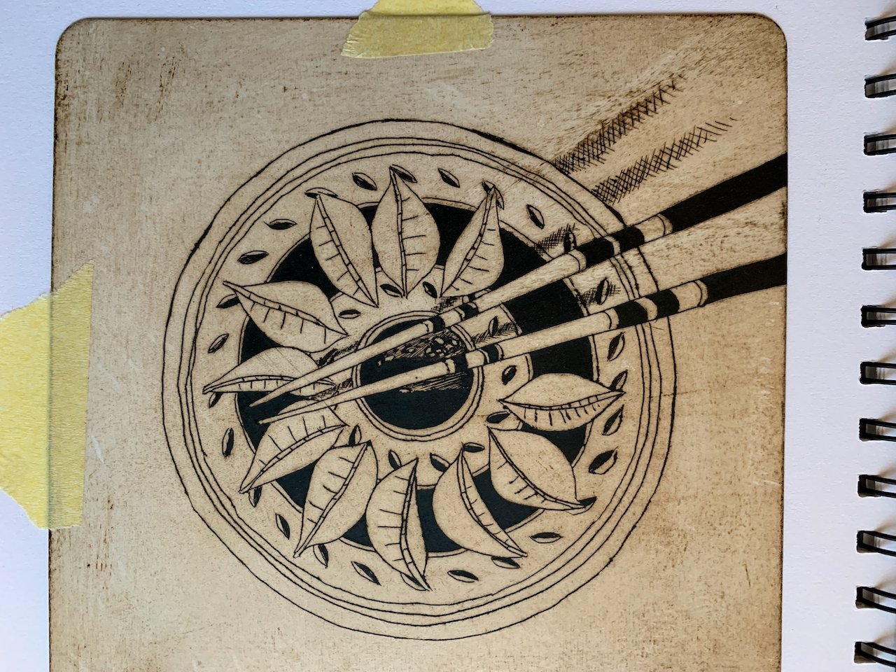 Line drawing of chopsticks resting on a decorative plate with leaves, set on a wooden surface.