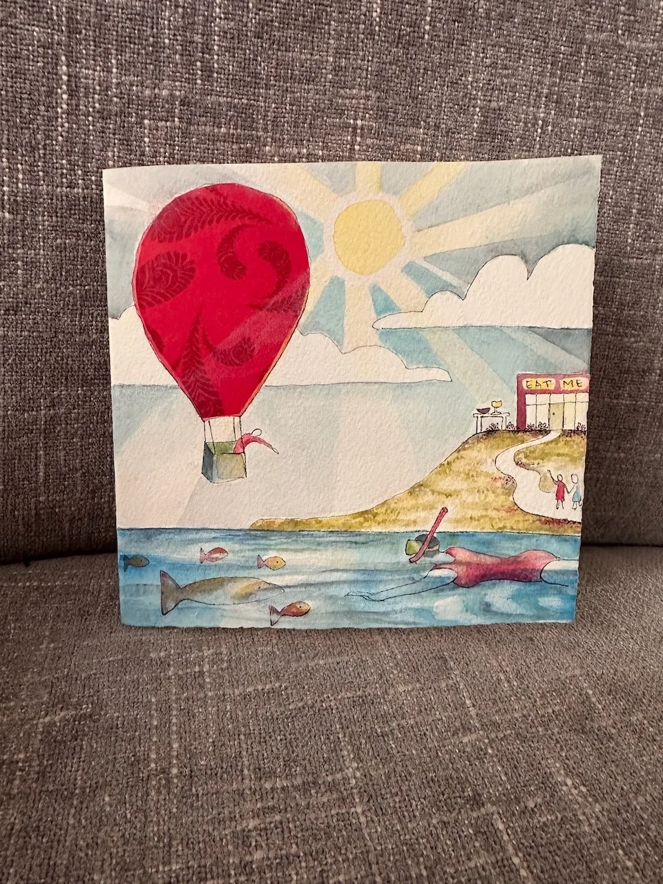 A watercolor painting of a seaside scene with a hot air balloon, fish in the water, and a couple walking near a restaurant that has a sign saying 'EAT ME'.
