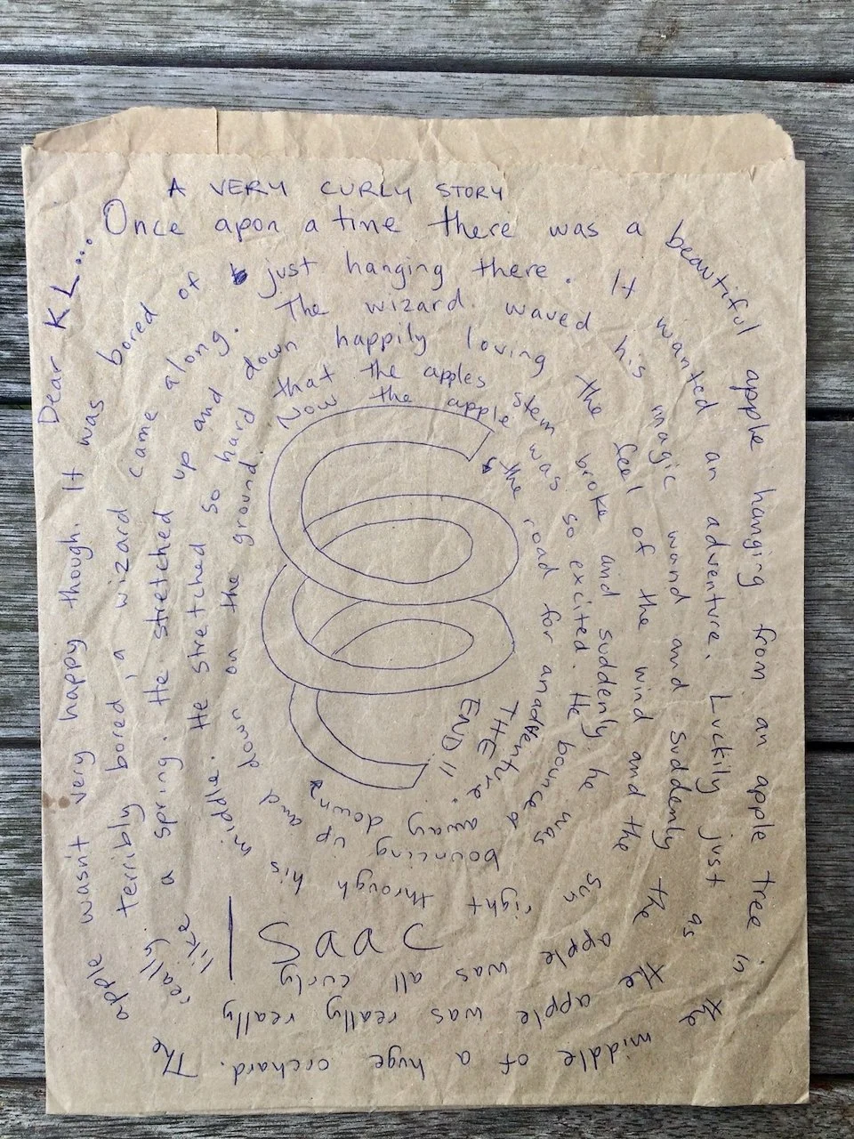 Handwritten story about a wizard, apples, and a curly design in the center on crumpled paper.
