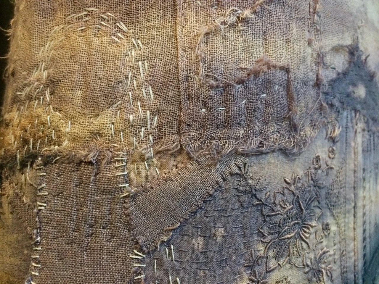 Close-up of a patchwork textile with various stitched fabric pieces, including embroidery and rough stitching.