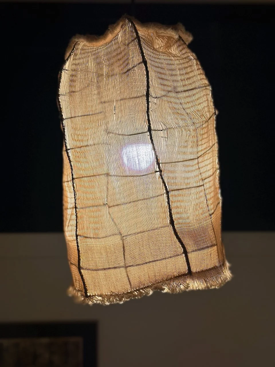 Close-up of a fabric lampshade with light shining through it, revealing the weave pattern and black seam lines.