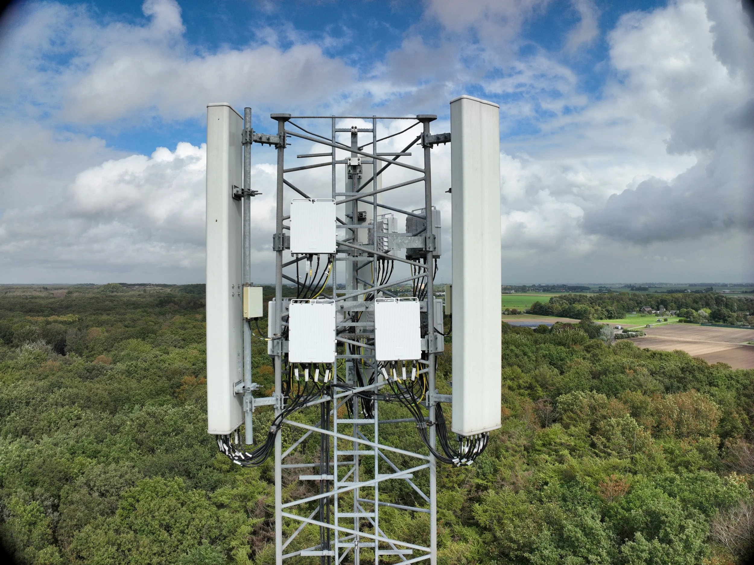 Een mobiele zendmast met meerdere antennes op een groene weide onder een bewolkte hemel.
