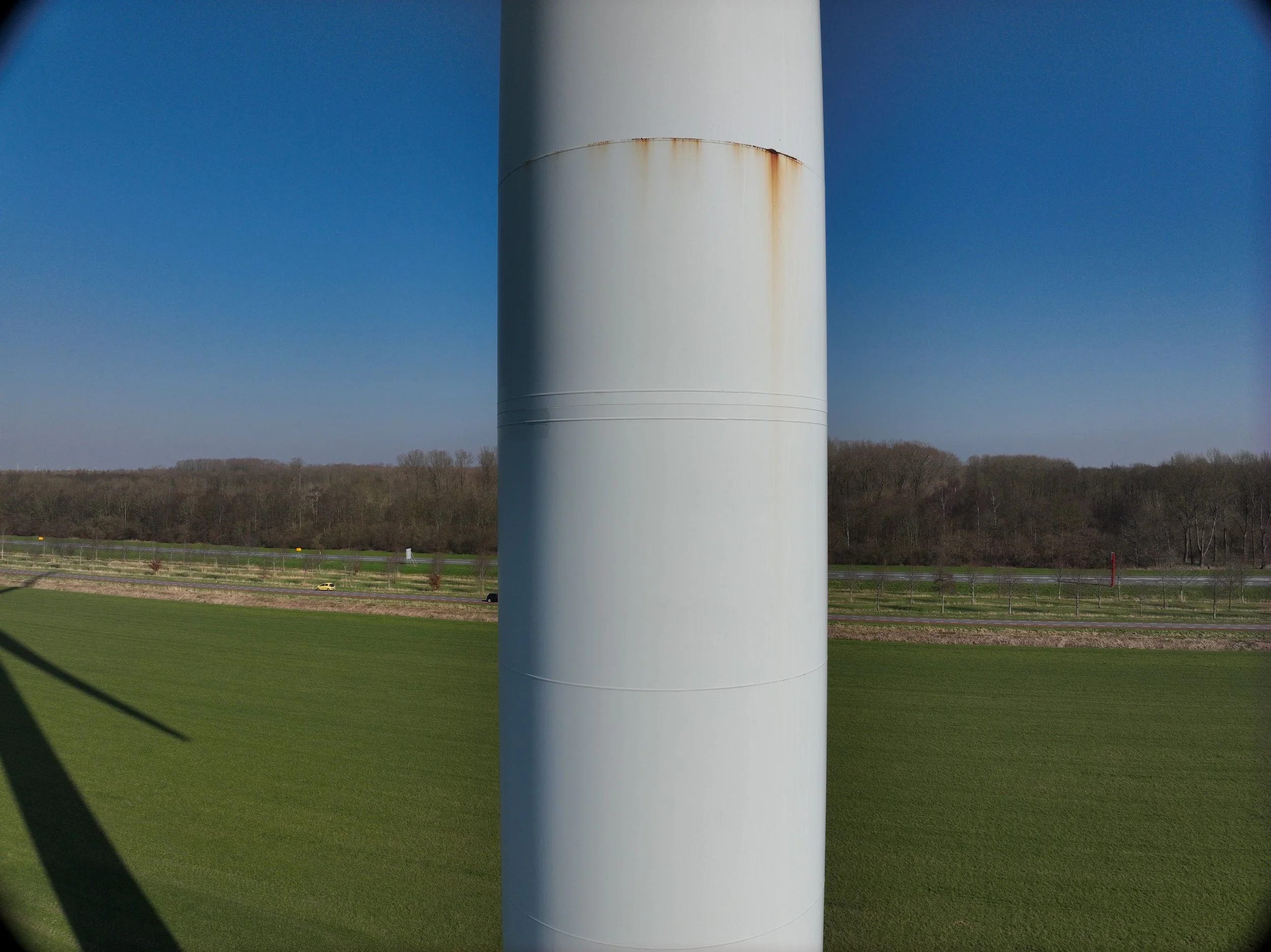 Een grote witte windturbine staat in een groen landschap onder een blauwe hemel.
